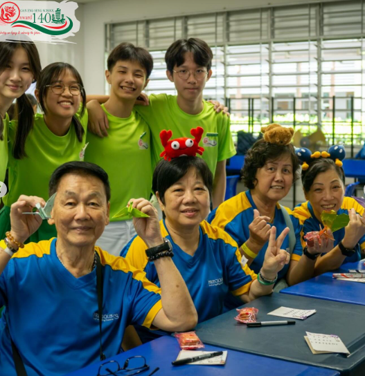 Group of people in blue-yellow and green shirts smiling at camera, some wearing fun accessories like a red crab headband.