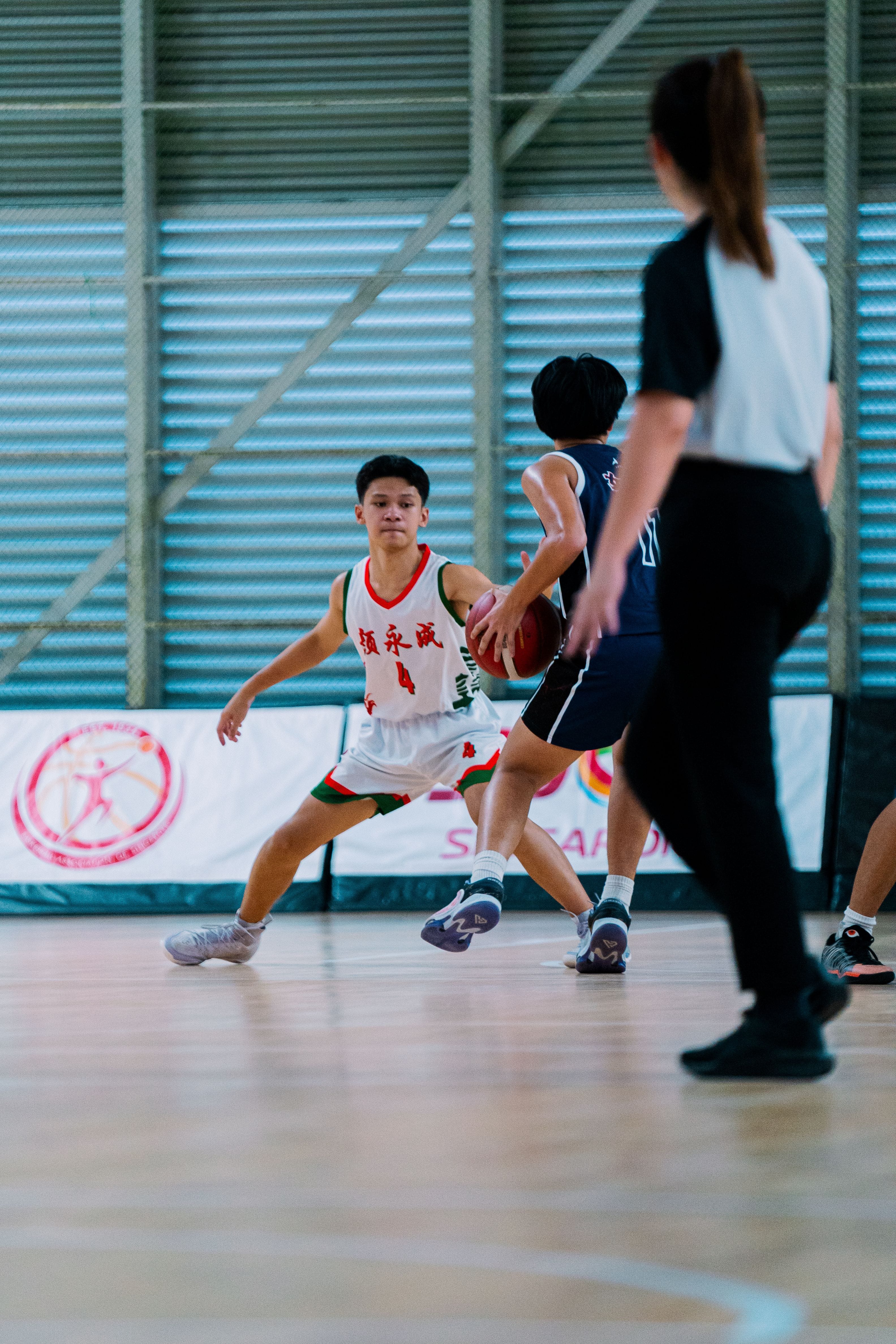 Player in white jersey number 4 defends against a navy-uniformed opponent holding a basketball indoors.