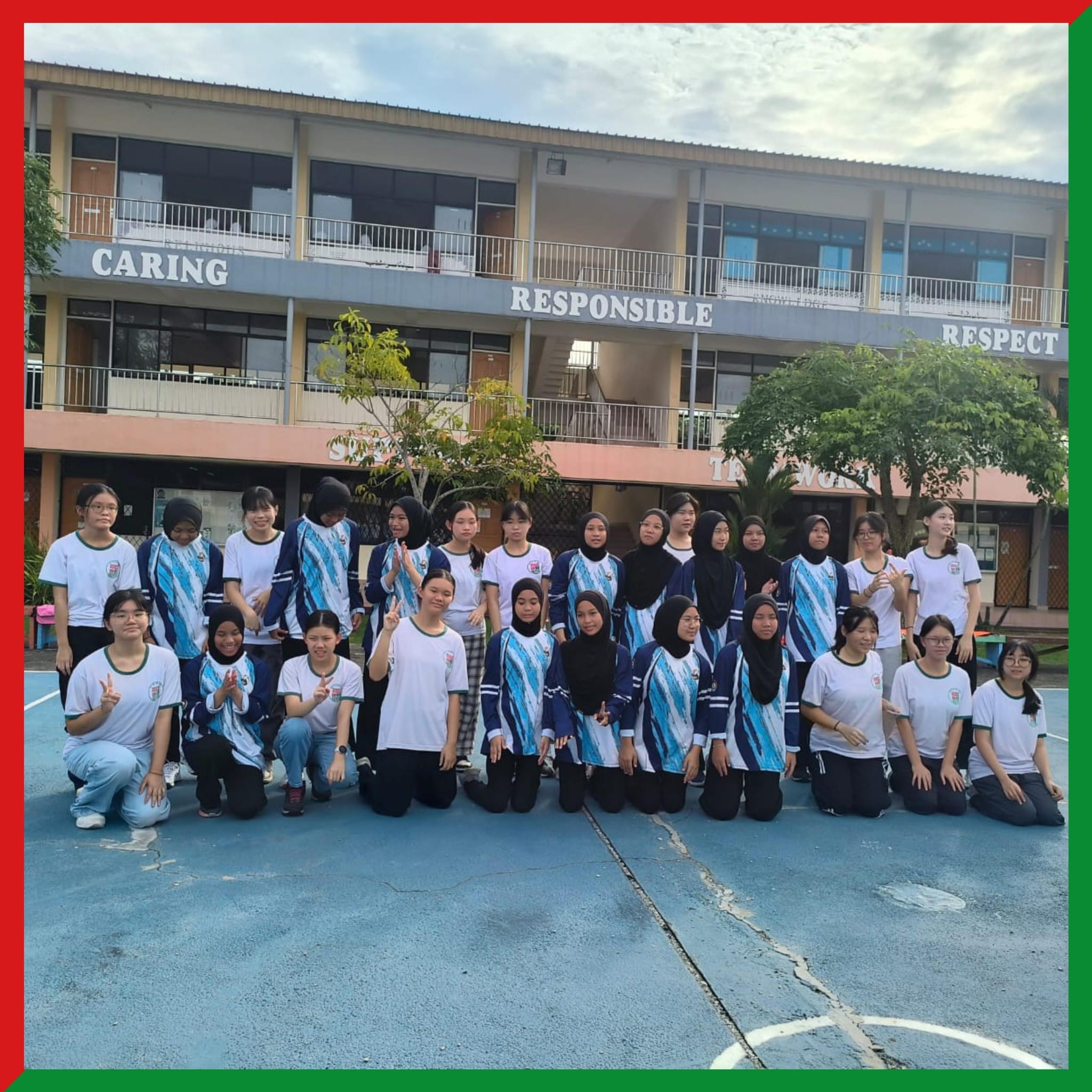 A group of female students in uniforms pose on a school courtyard in front of a building labeled Caring, Responsible, Respect.