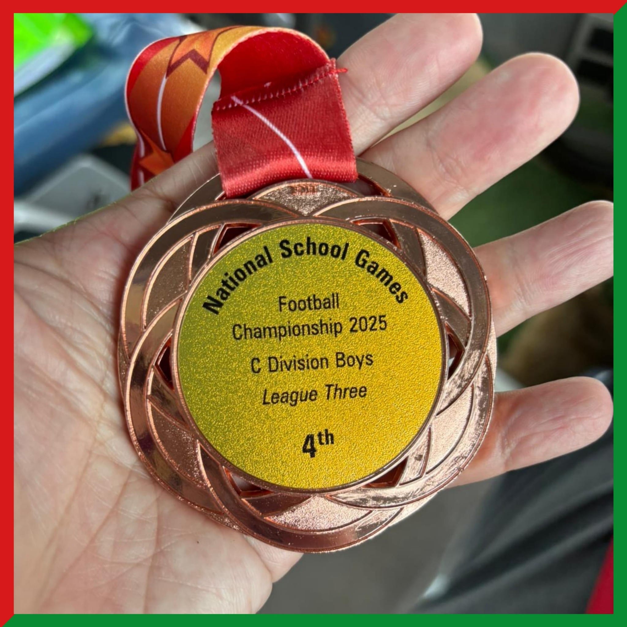 A hand holds a bronze medal reading National School Games Football Championship 2025 C Division Boys League Three 4th.