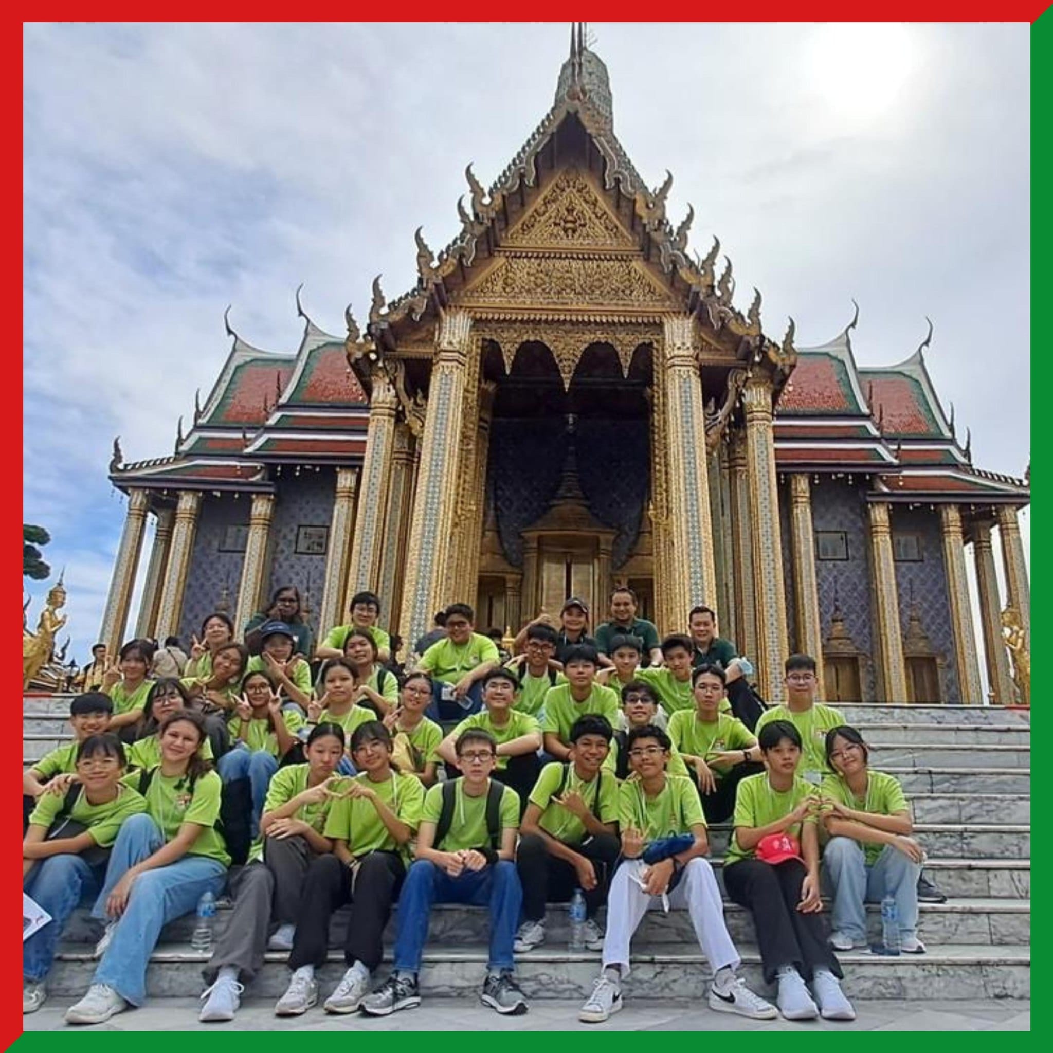 A large group of young people in green shirts pose on steps in front of an ornate Thai temple with golden decorations.
