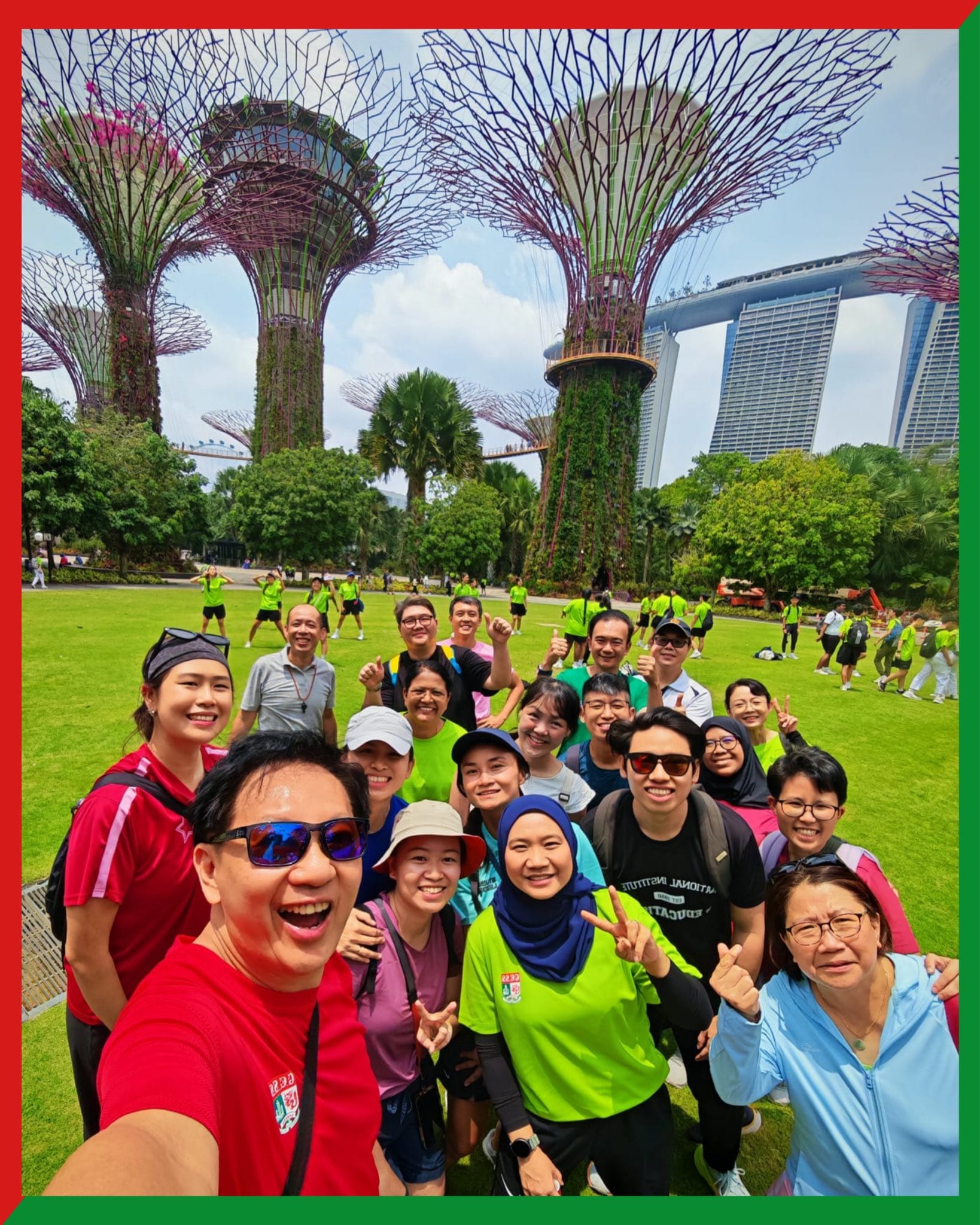 A smiling group takes a selfie at Gardens by the Bay, Singapore, with Supertrees and Marina Bay Sands behind them.