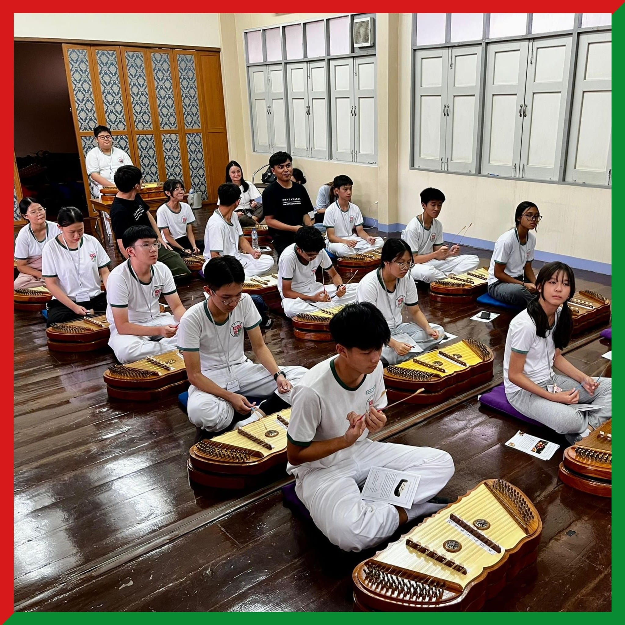 Students in white uniforms sit cross-legged on a wooden floor, each with a traditional string instrument in front of them.