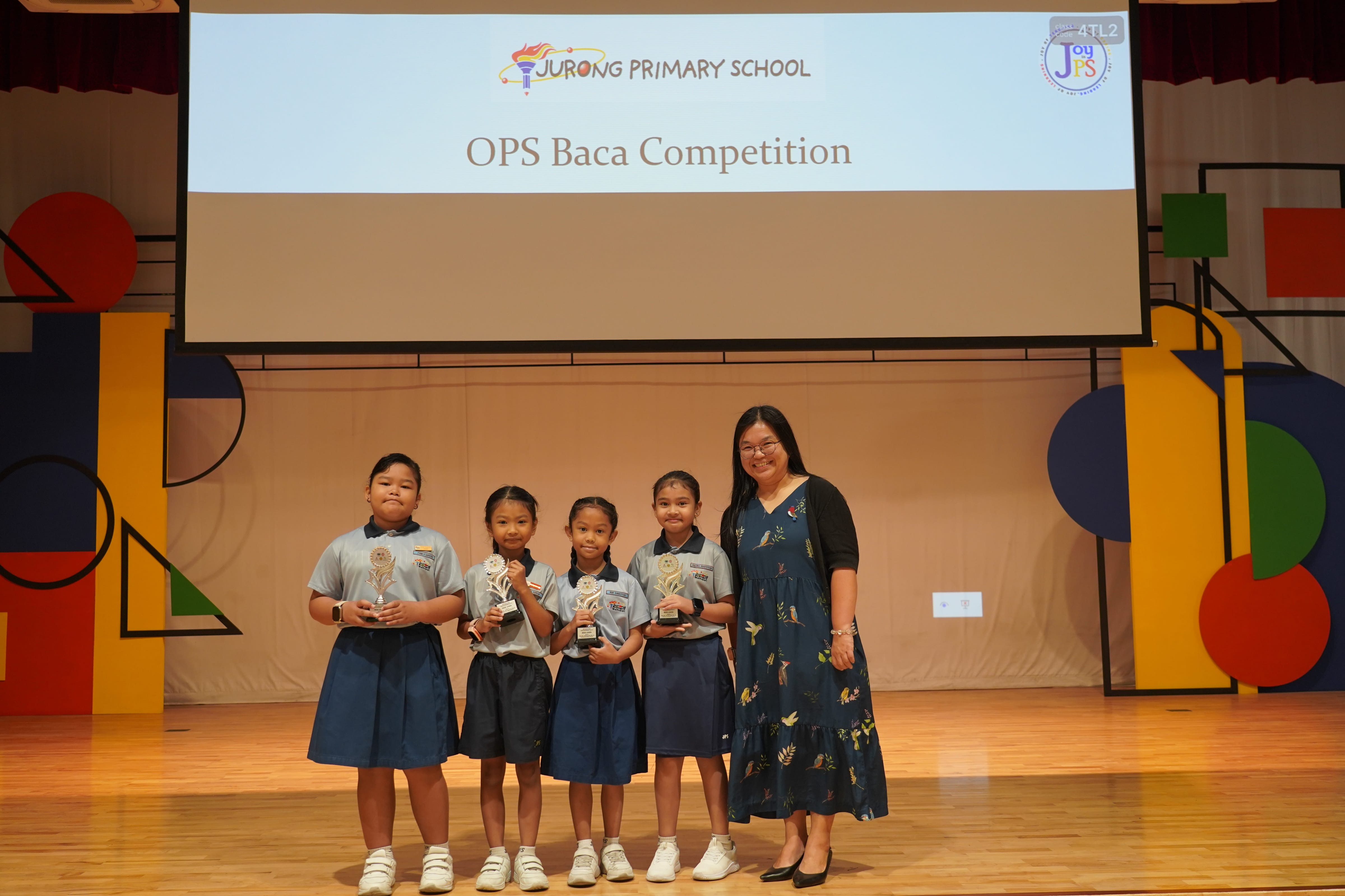 Four young students holding trophies with a Vice-Principal on stage at OPS Baca Competition.