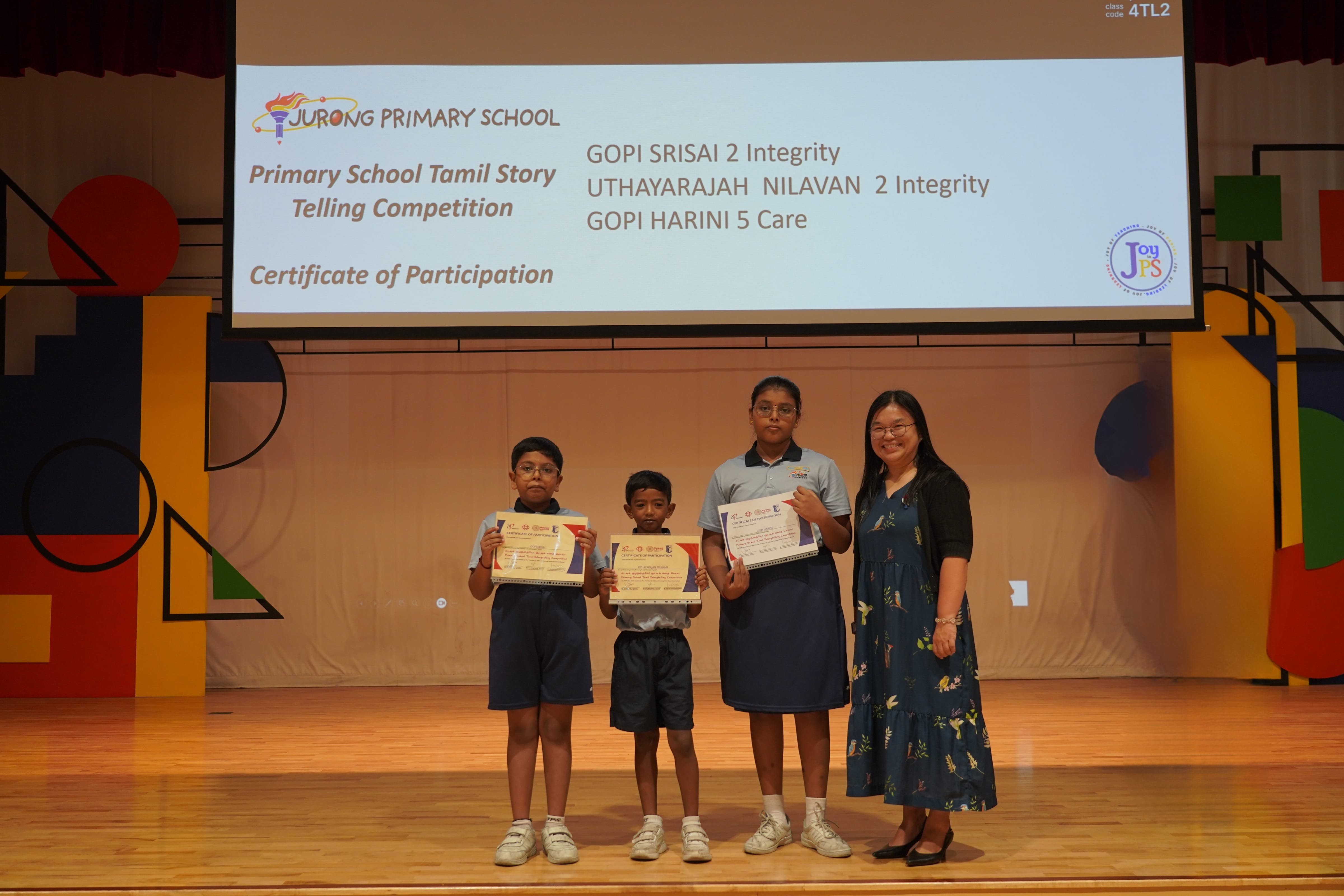 Three students holding participation certificates with a Vice-Principal, Tamil Story Telling Competition.