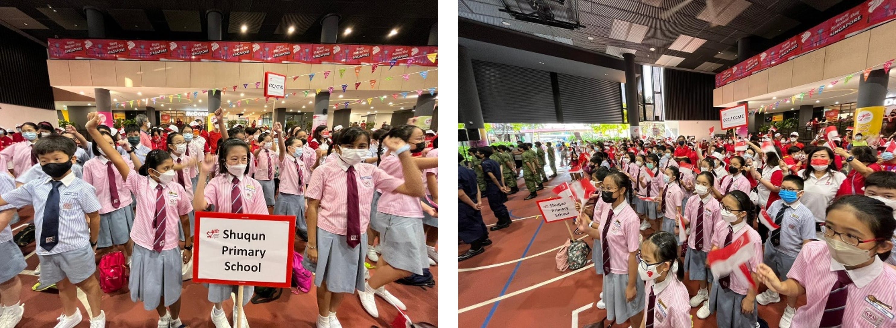 Students in pink uniforms from Shuqun Primary School gather indoors waving Singapore flags at a National Day event.