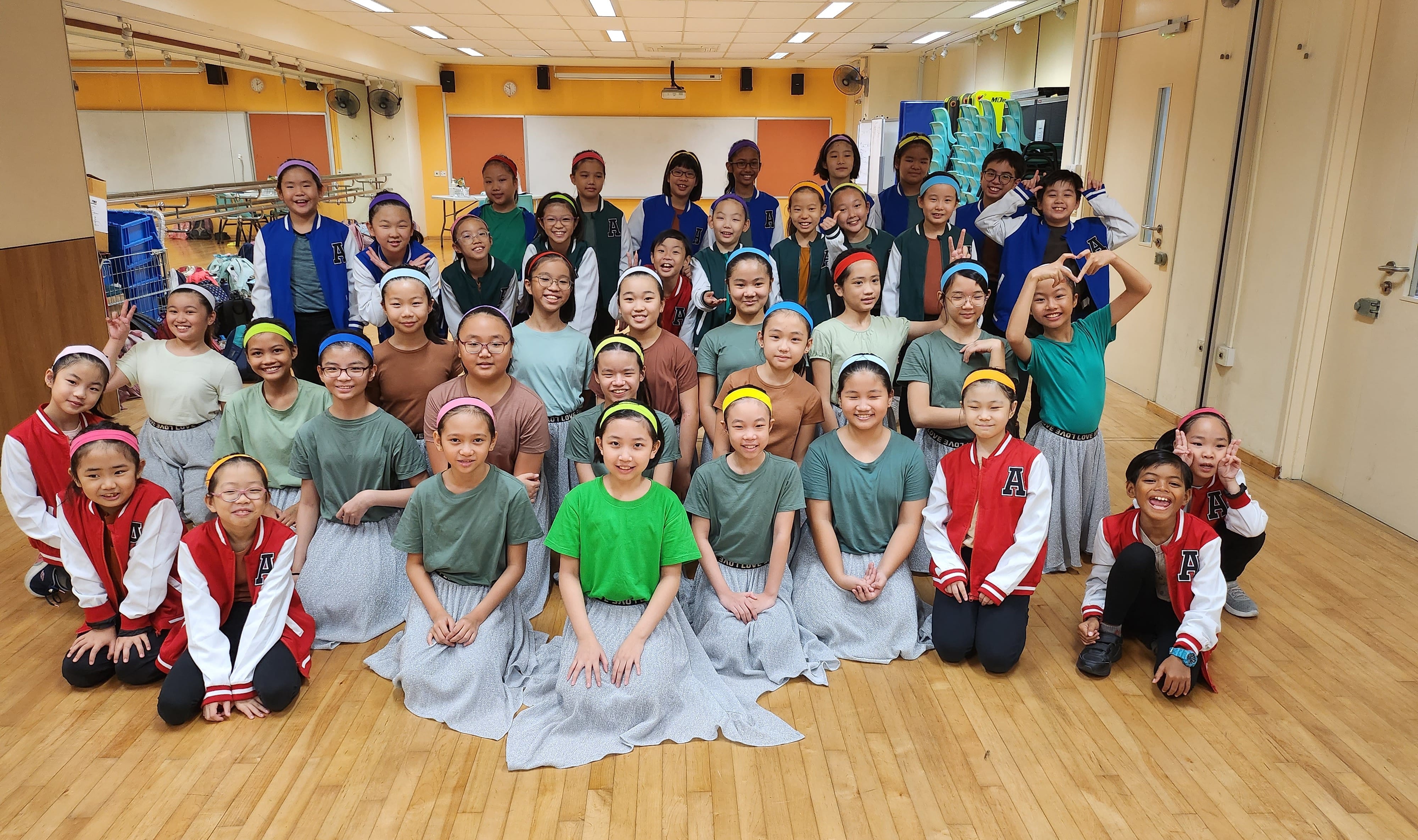A large group of children in colorful headbands and matching outfits pose together in a school gymnasium.