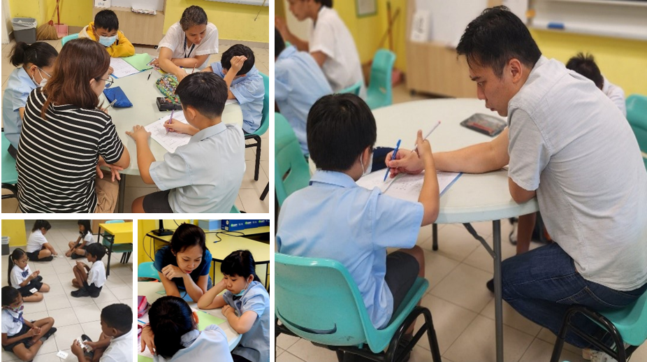 Adults and children in school uniforms sit at tables and on floors in a classroom, working together on activities.