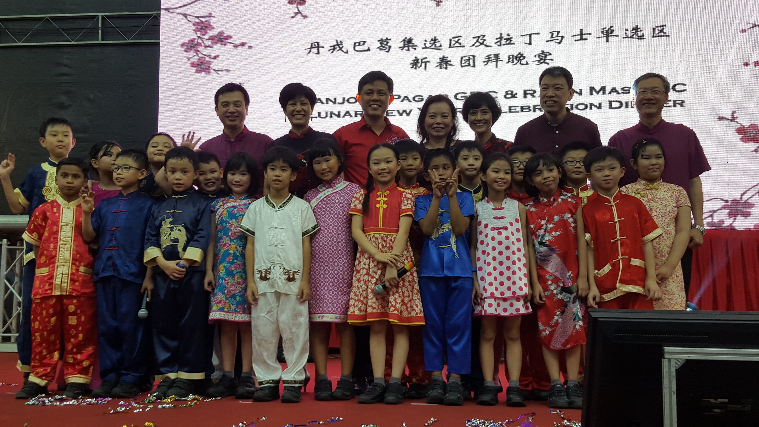 MPs with adults and children in traditional Chinese outfits pose on stage at a Lunar New Year celebration dinner.