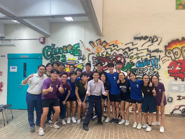 A group of students and two adults pose together in front of a colorful graffiti mural indoors.
