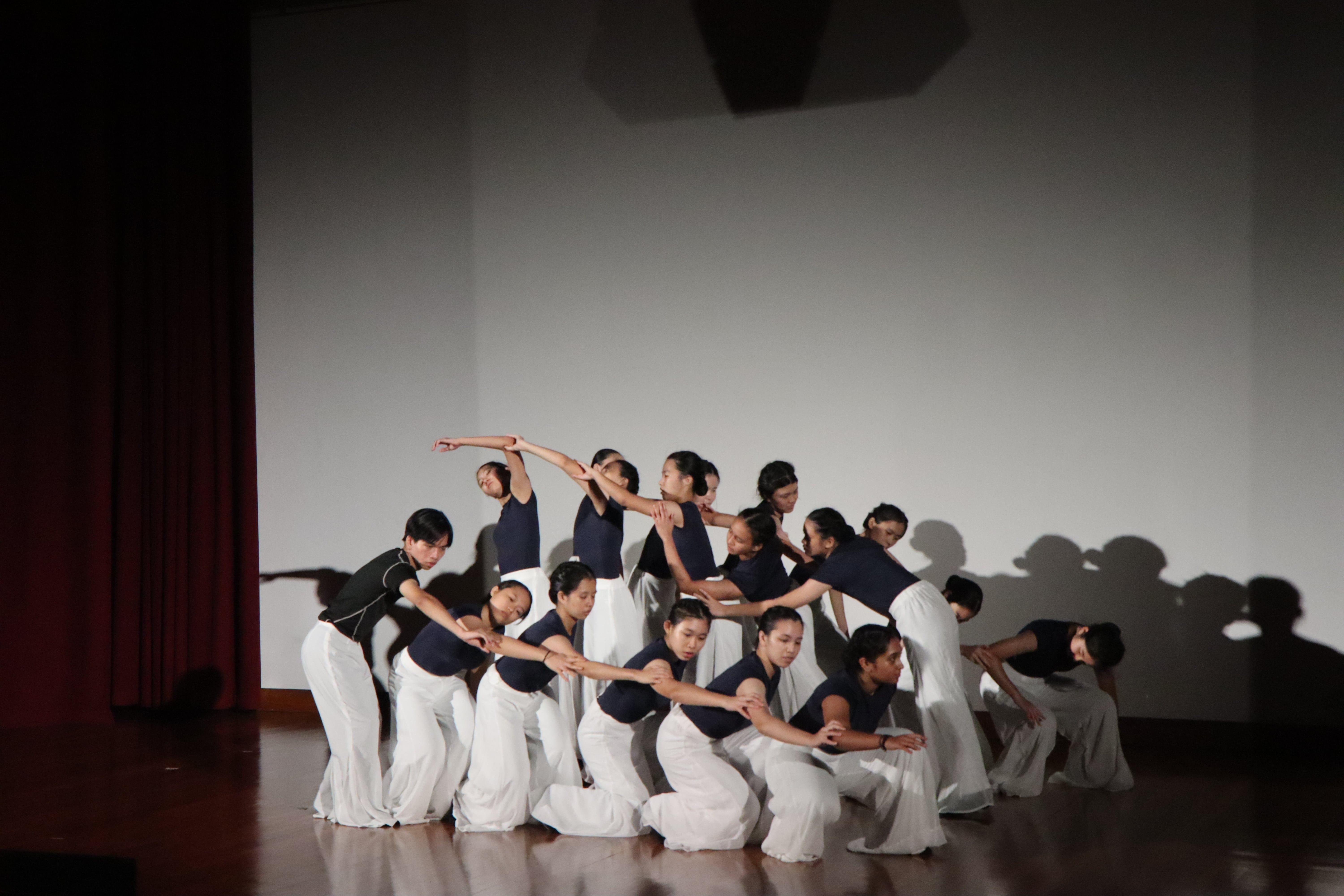 A group of dancers in navy tops and white pants perform a synchronized routine on a stage.