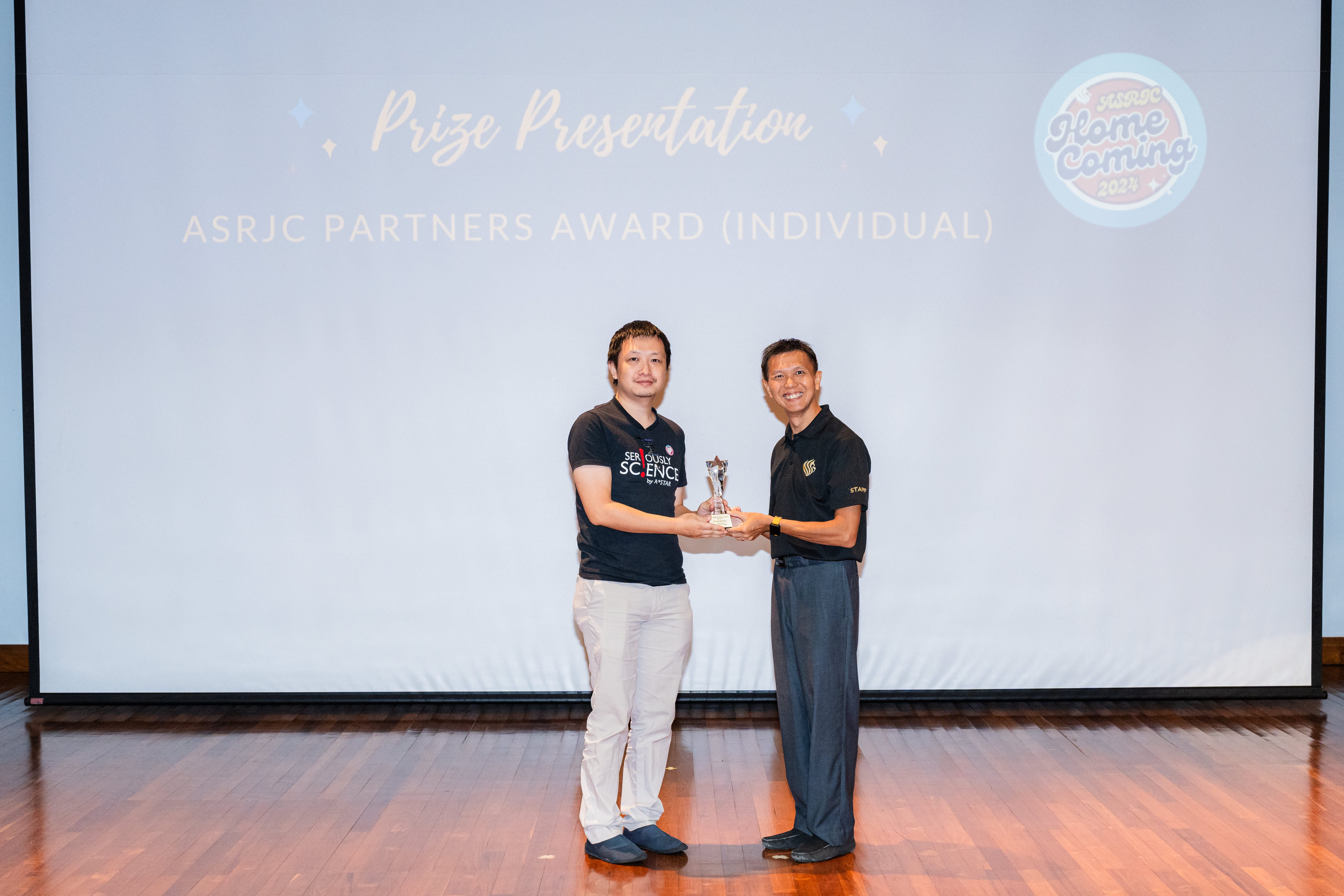 Two men stand on a stage holding a trophy together during the ASRJC Partners Award Individual prize presentation.