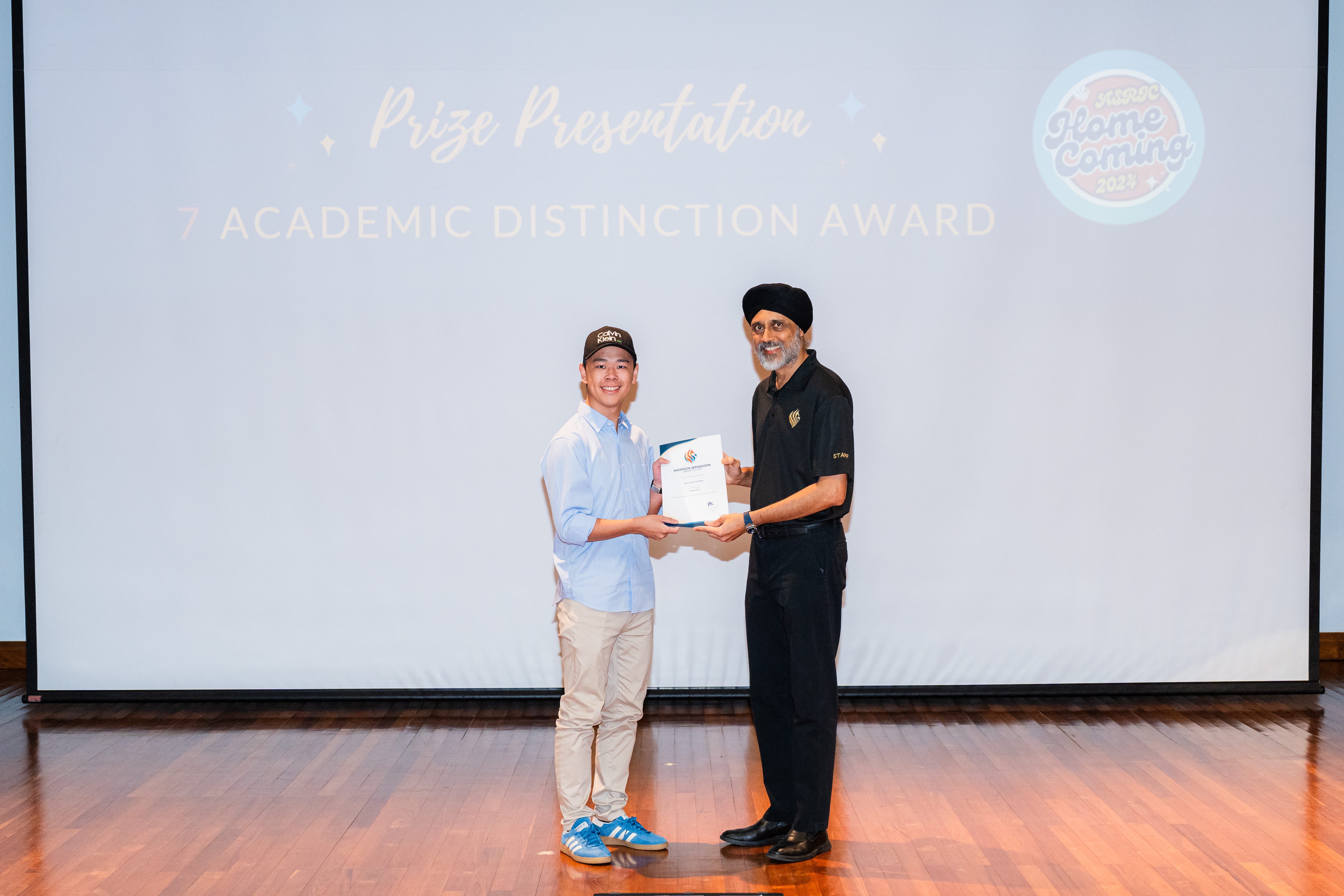 Two people onstage hold a certificate; behind them reads Prize Presentation and Academic Distinction Award.