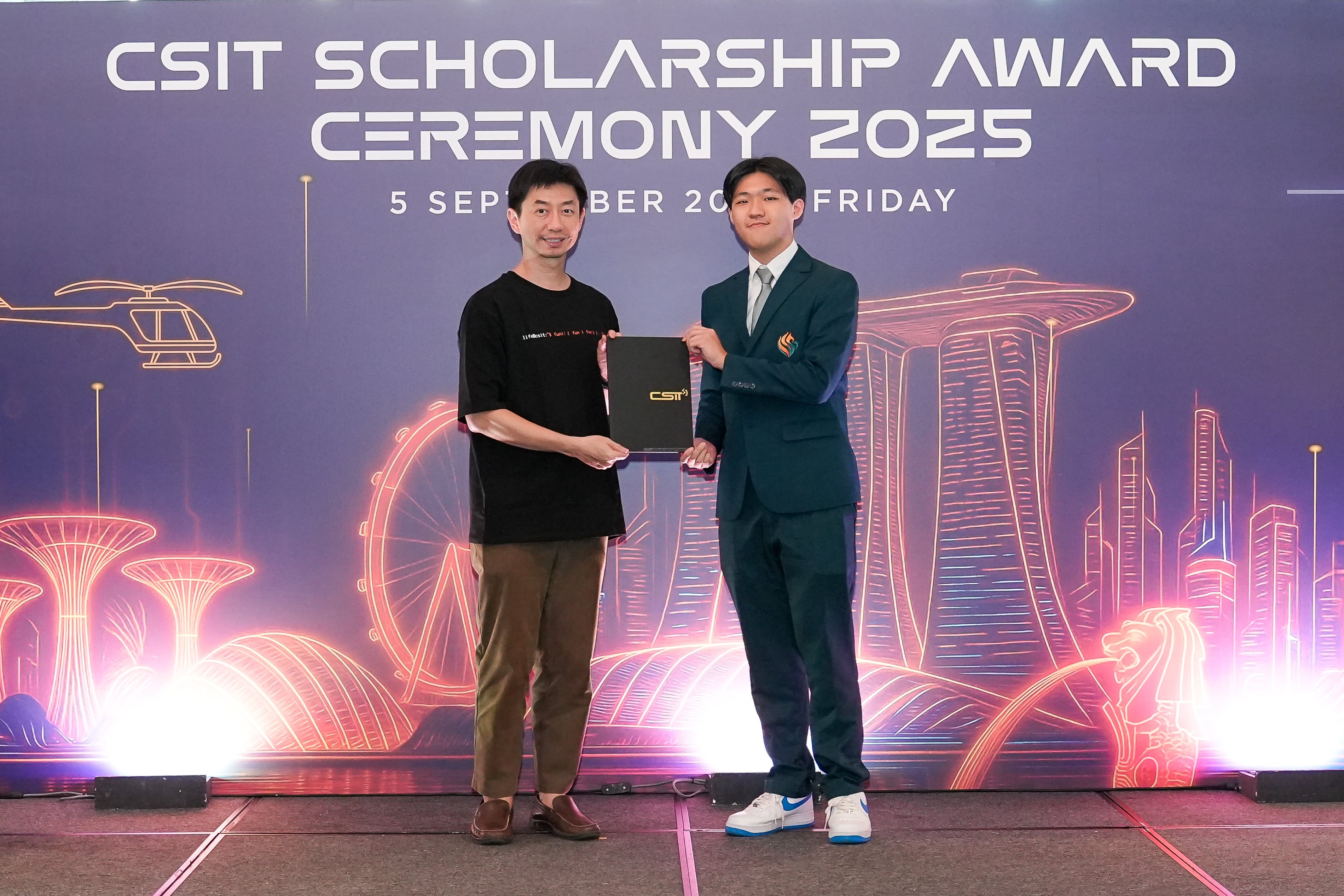 Two men hold a black folder on stage at the CSIT Scholarship Award Ceremony 2025 on 5 September.
