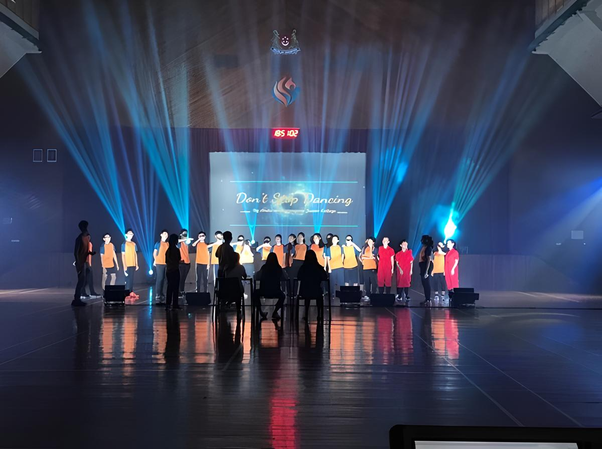 A group of AVA students on a lit stage with blue beams and a screen reading "Don't Stop Dancing."
