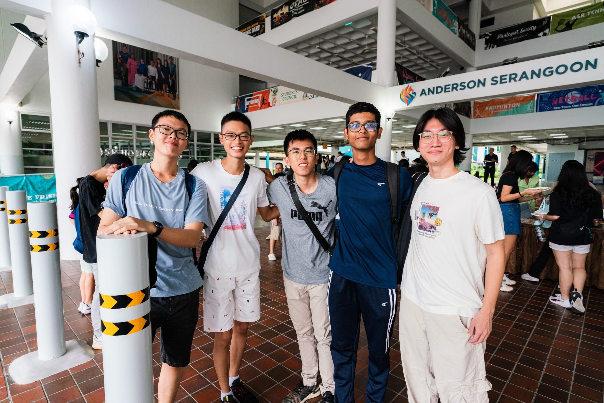 Five young men smile together in a school corridor with an Anderson Serangoon sign visible above.