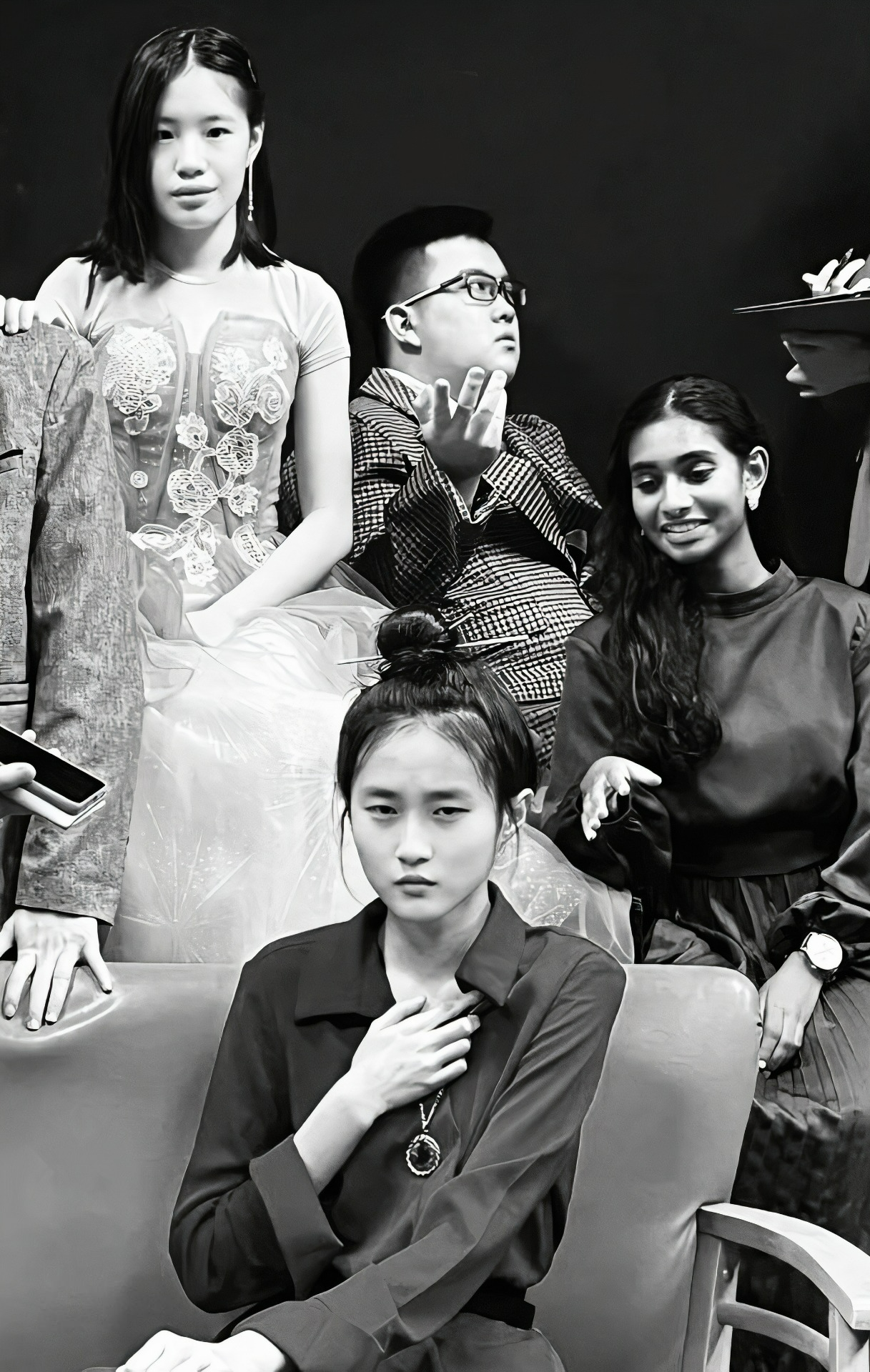Black and white photo of four young people seated and standing, one woman in a floral dress, another in a dark blazer.