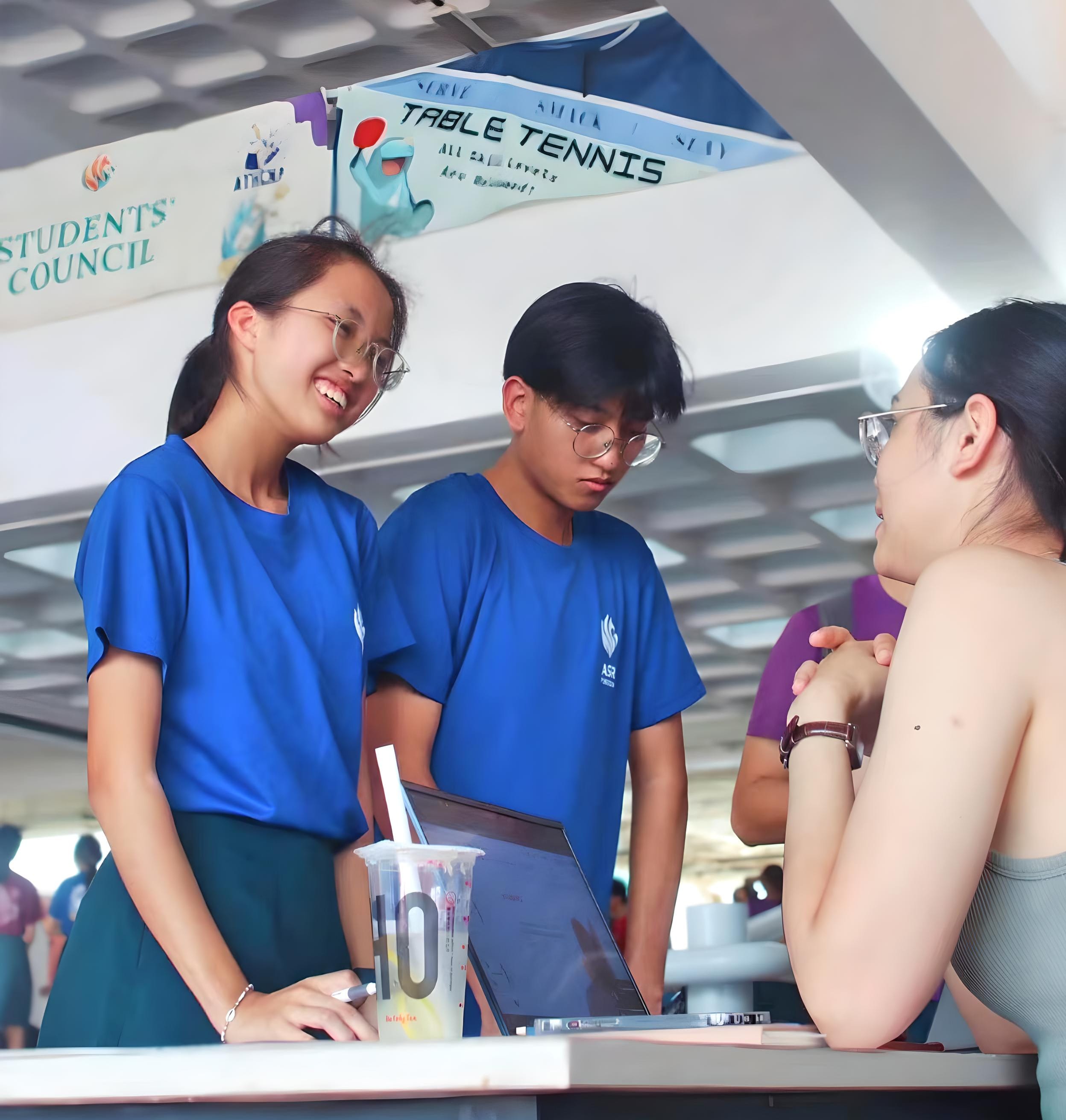 Two students in blue shirts stand at a booth