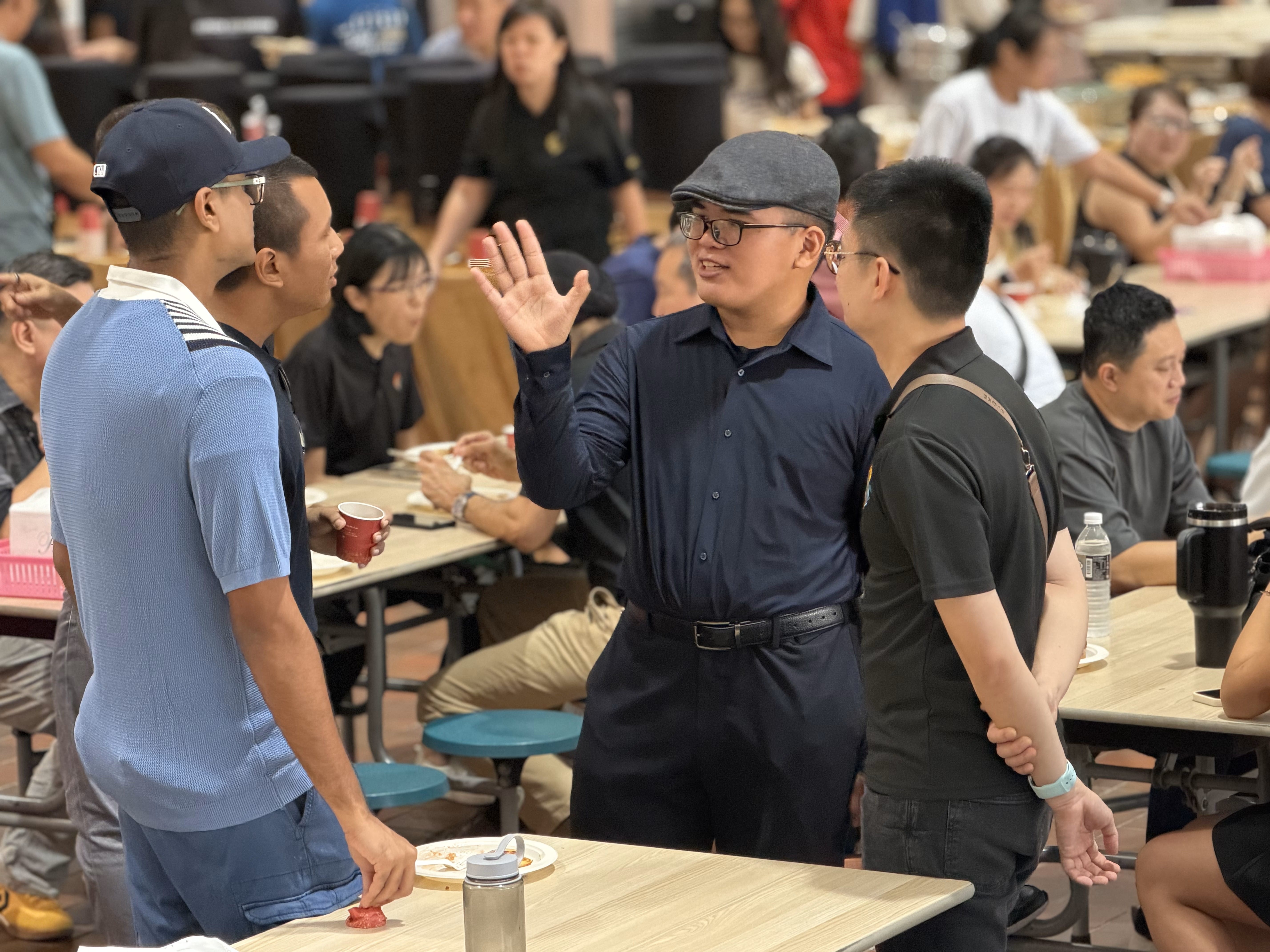 2 men in blue and wearing caps talk to a man in black in the canteen