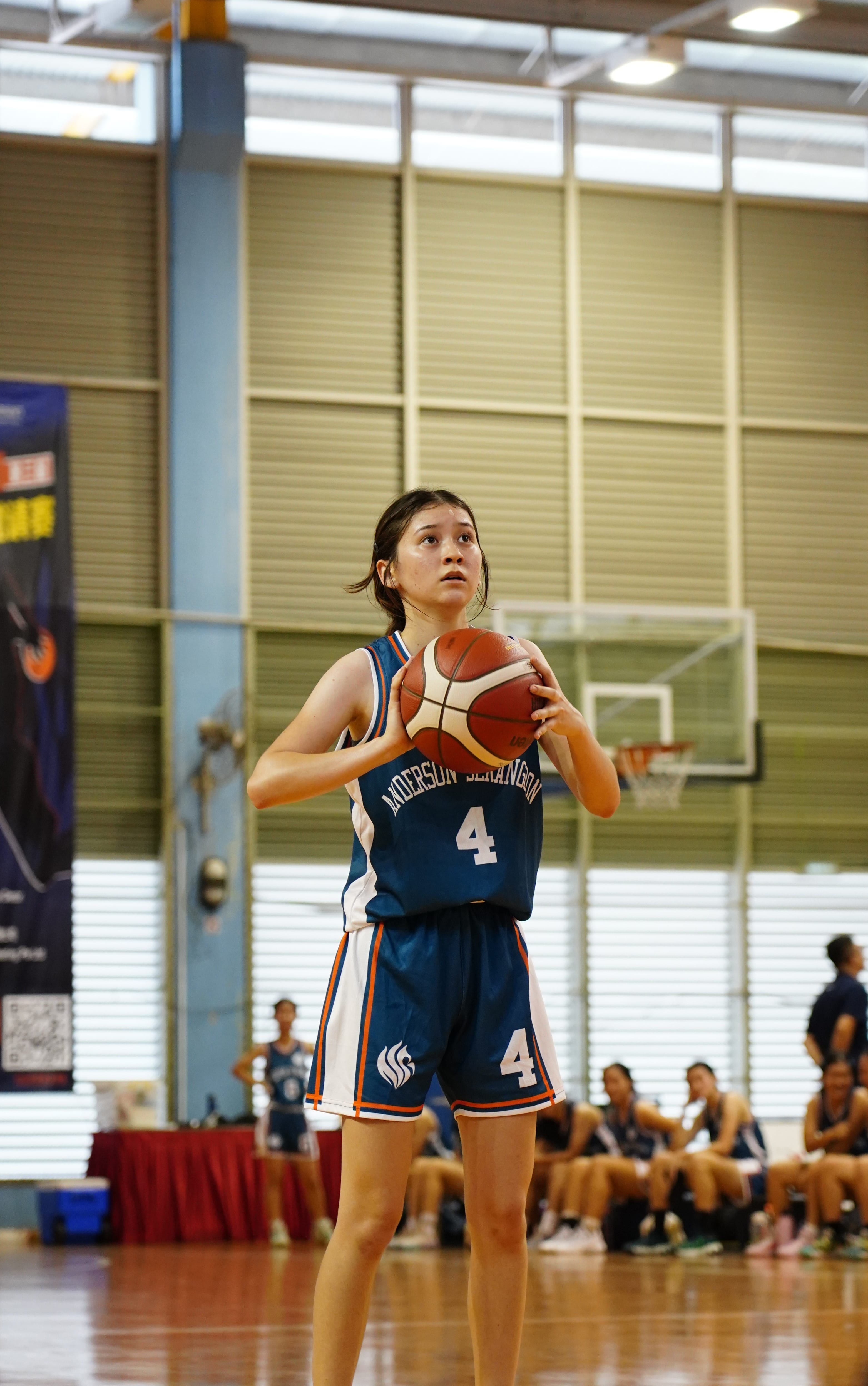 Young female basketball player wearing number 4 blue jersey prepares to shoot indoors at a gymnasium.