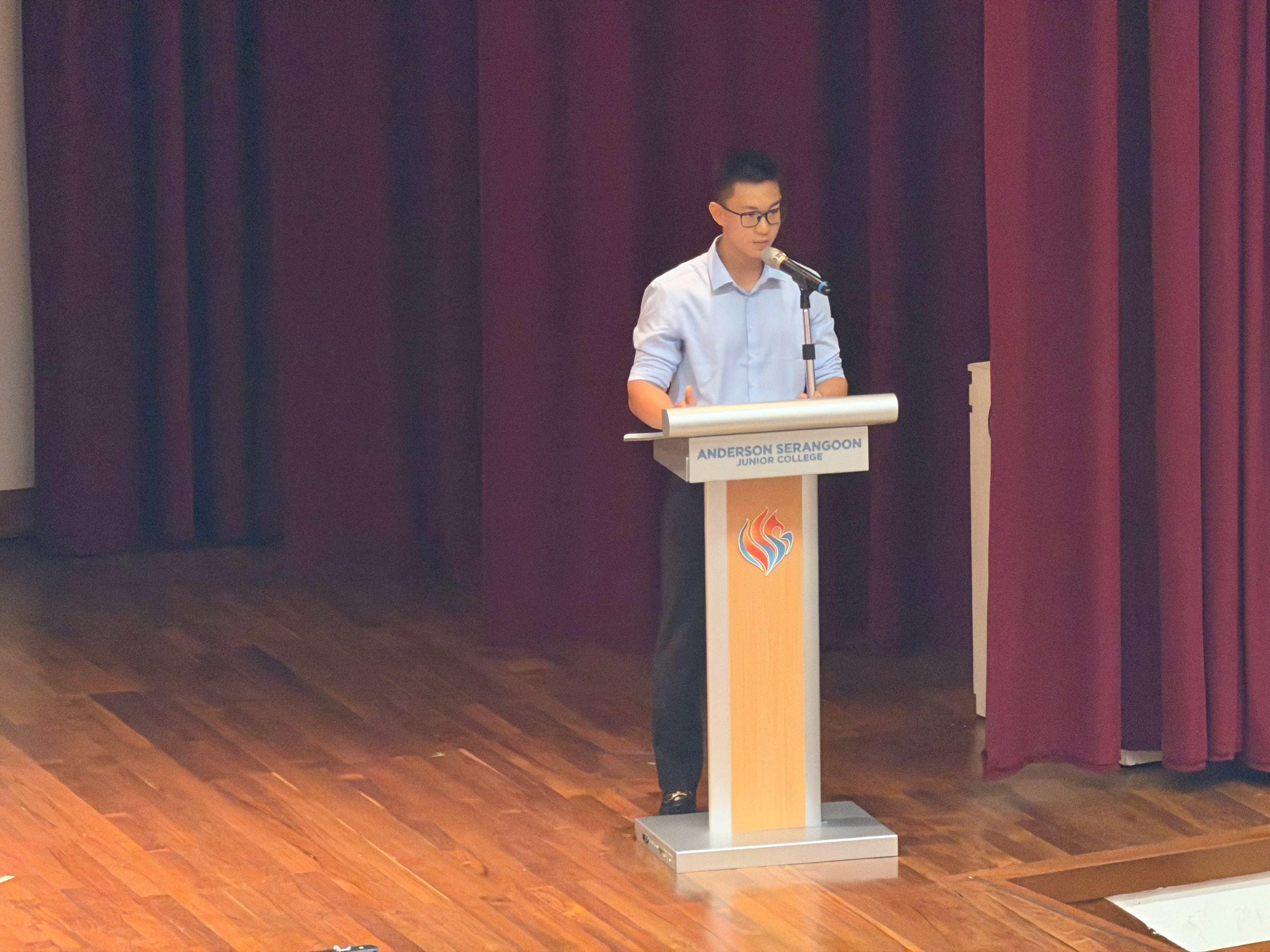 A male student in light blue shirt stands on stage to speak to the audience