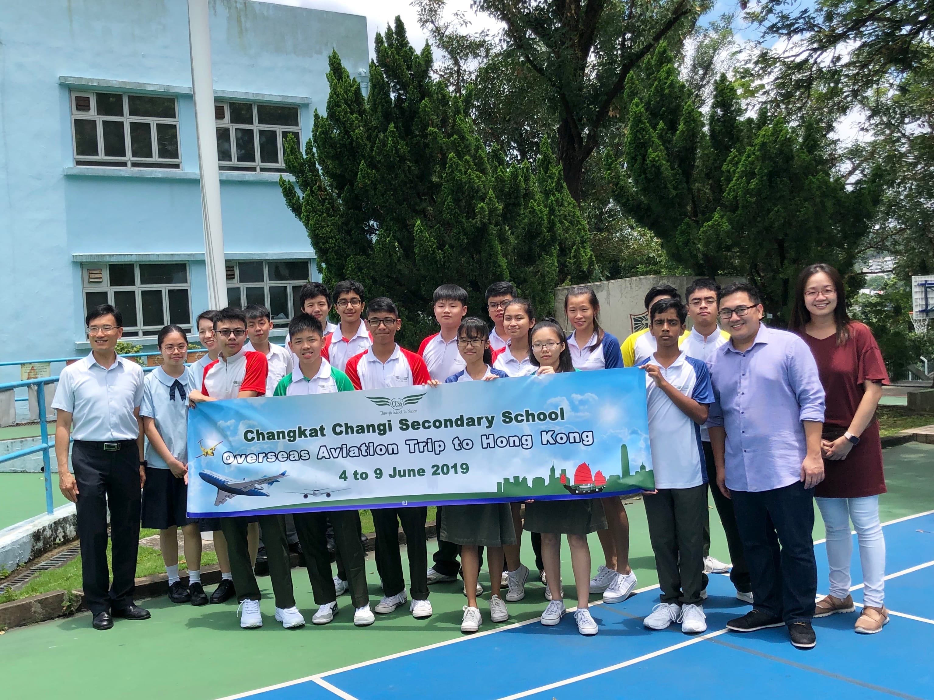 A group of students and teachers hold a banner reading Changkat Changi Secondary School Overseas Aviation Trip to Hong Kong, June 2019.