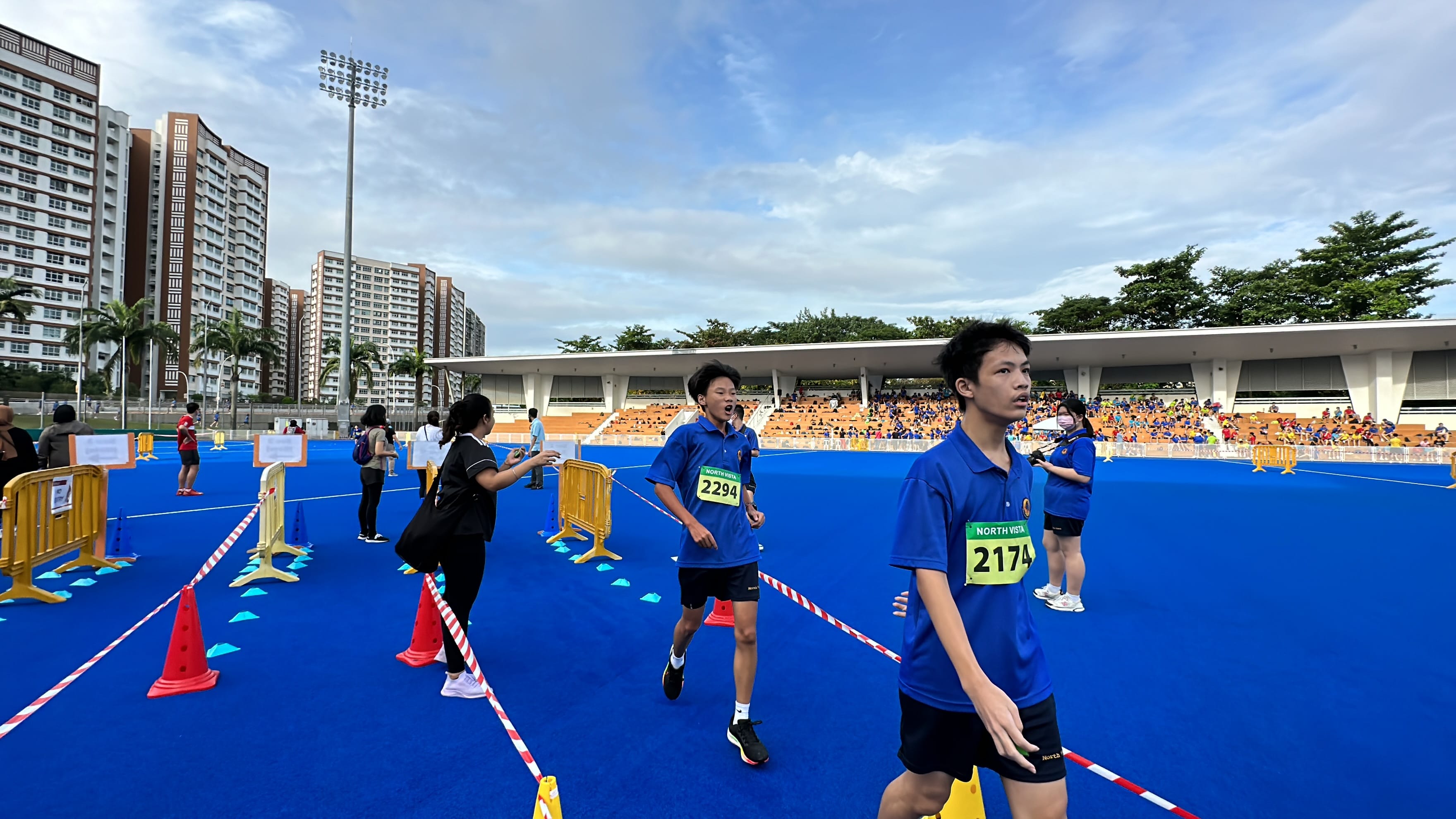 NV students with race bibs 2174 and 2294 walk on a blue outdoor track stadium.