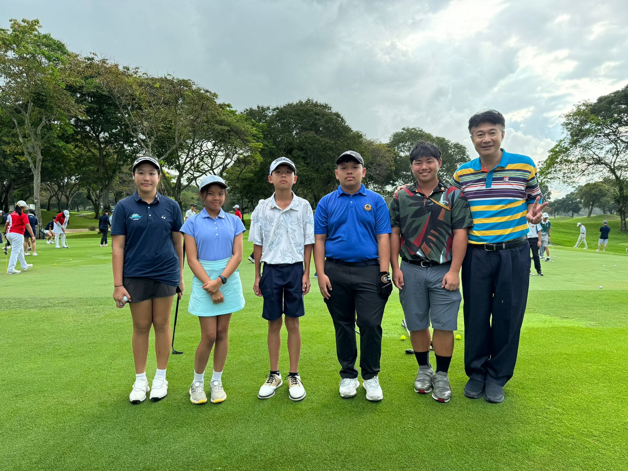 NV student golfers with teacher in charge pose together on a green golf course surrounded by trees.