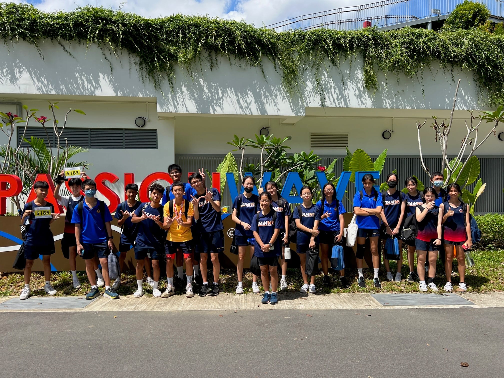 NV students pose in front of a Passion Wave sign on a sunny day.
