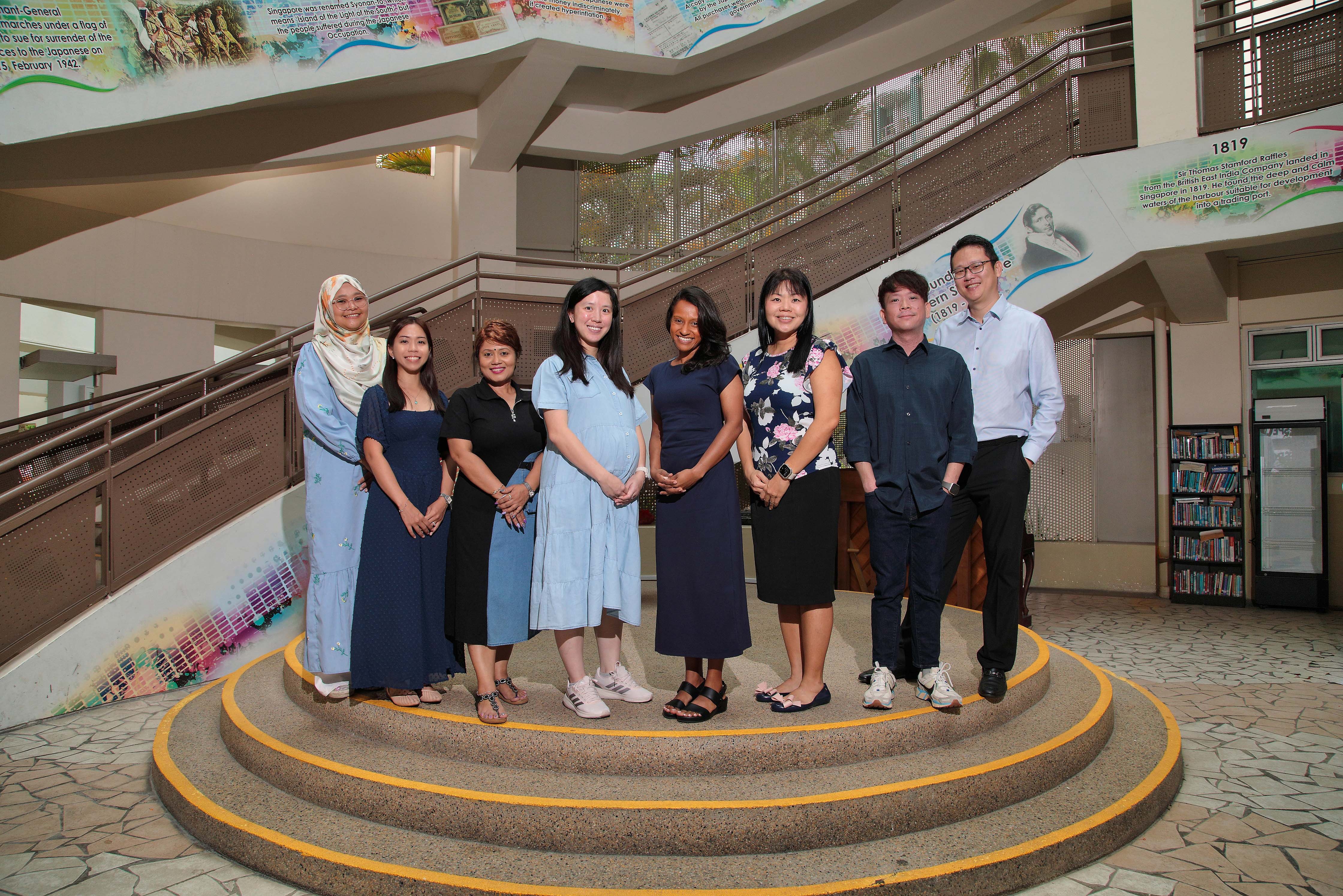NV Humanities department stand together on a raised circular platform inside a building with colorful history murals on the walls.