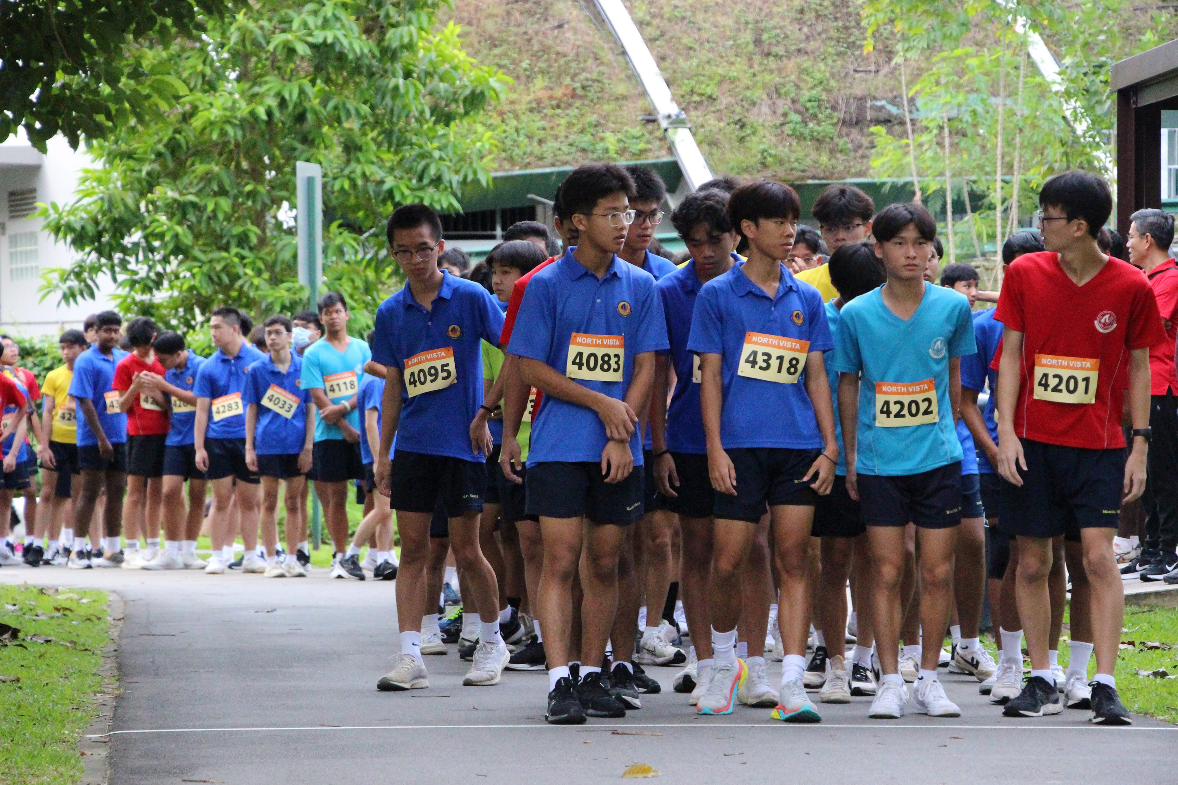 NV students wearing North Vista race bibs line up at the starting line of a school running event outdoors.