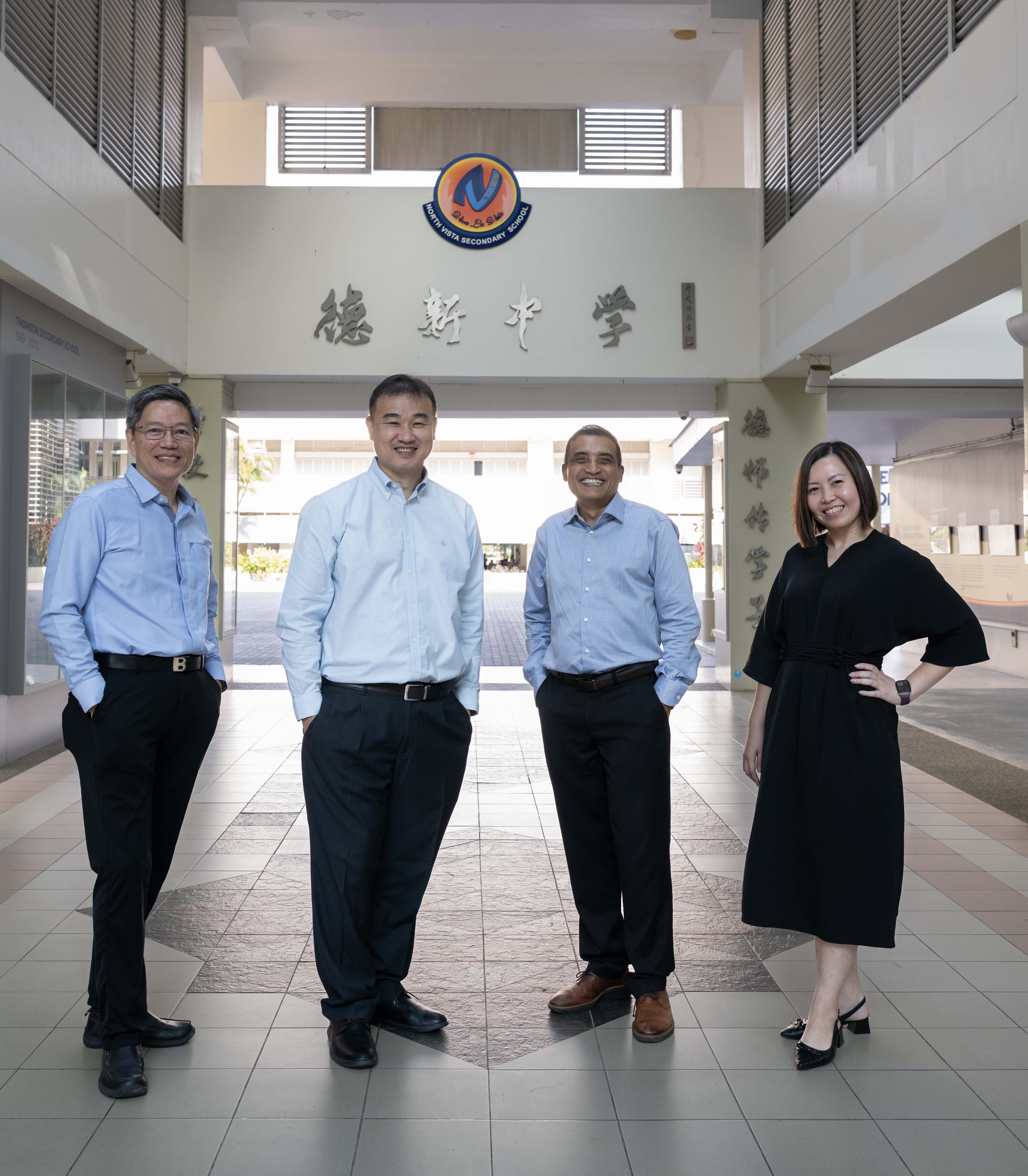 Four adults smiling and standing at the entrance of North Vista Secondary School with Chinese characters on the wall.