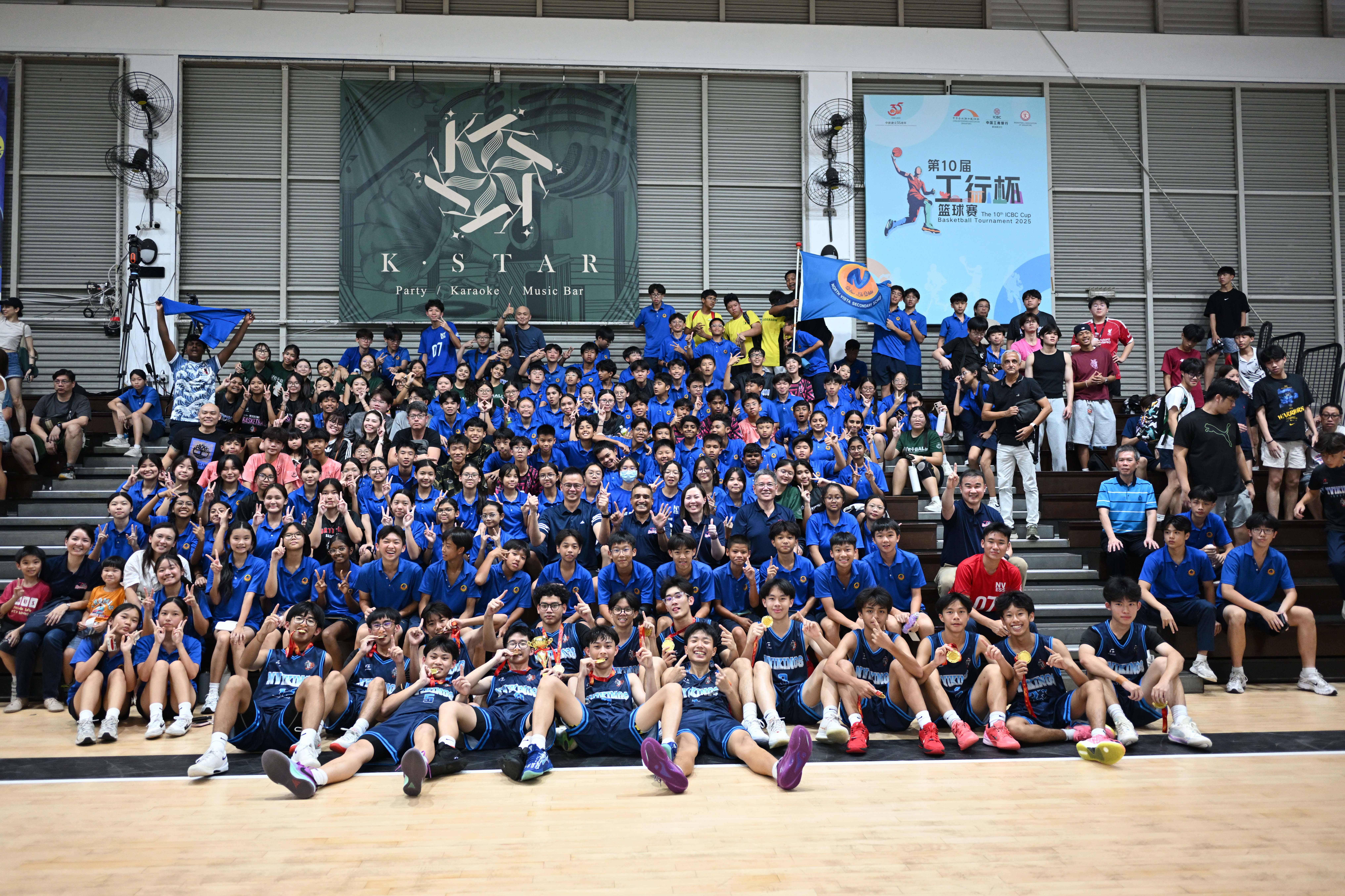 Large group photo of the North Vista basketball team and a crowd of cheering supporters (students) celebrating a victory in the indoor stadium.
