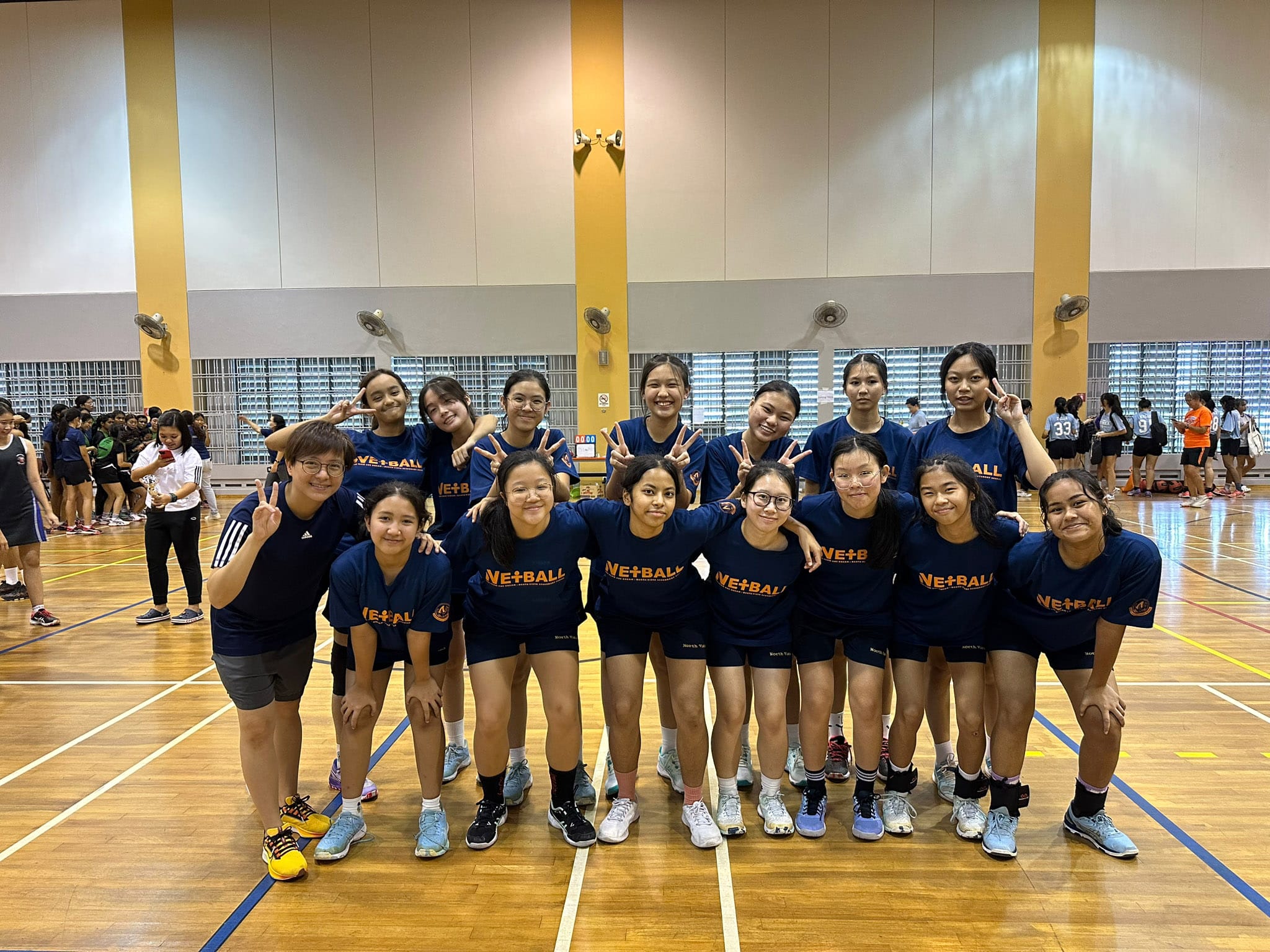 NV Netball players in navy blue Netball jerseys posing together in an indoor sports hall.