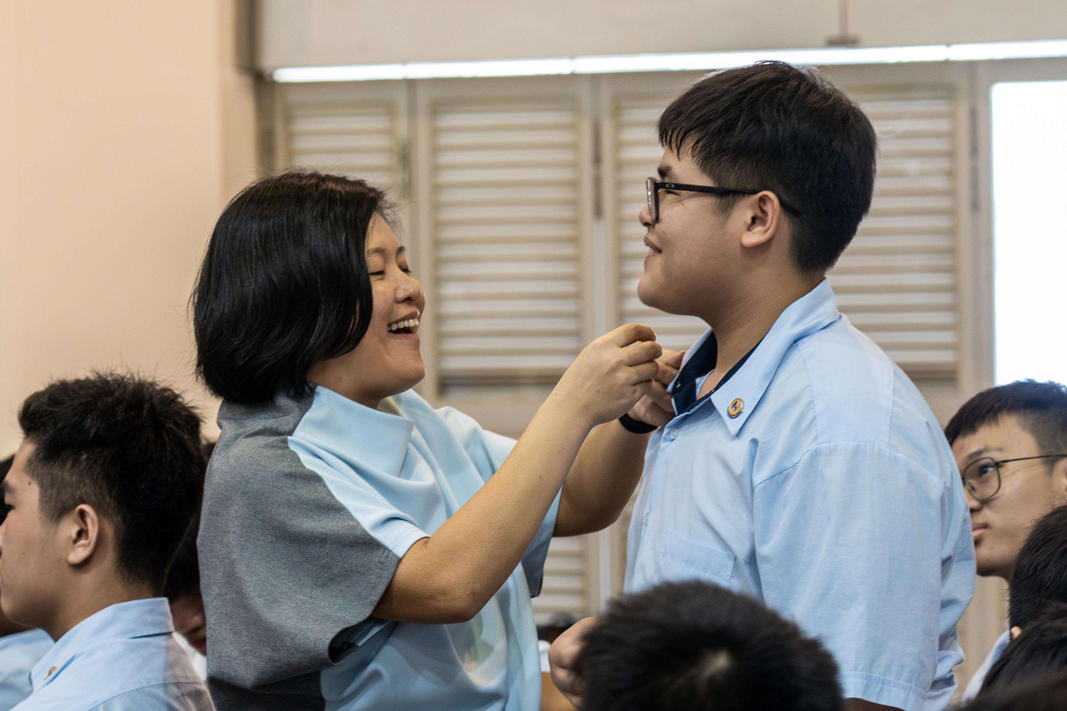 A teacher pins a badge onto her student's collar in hall