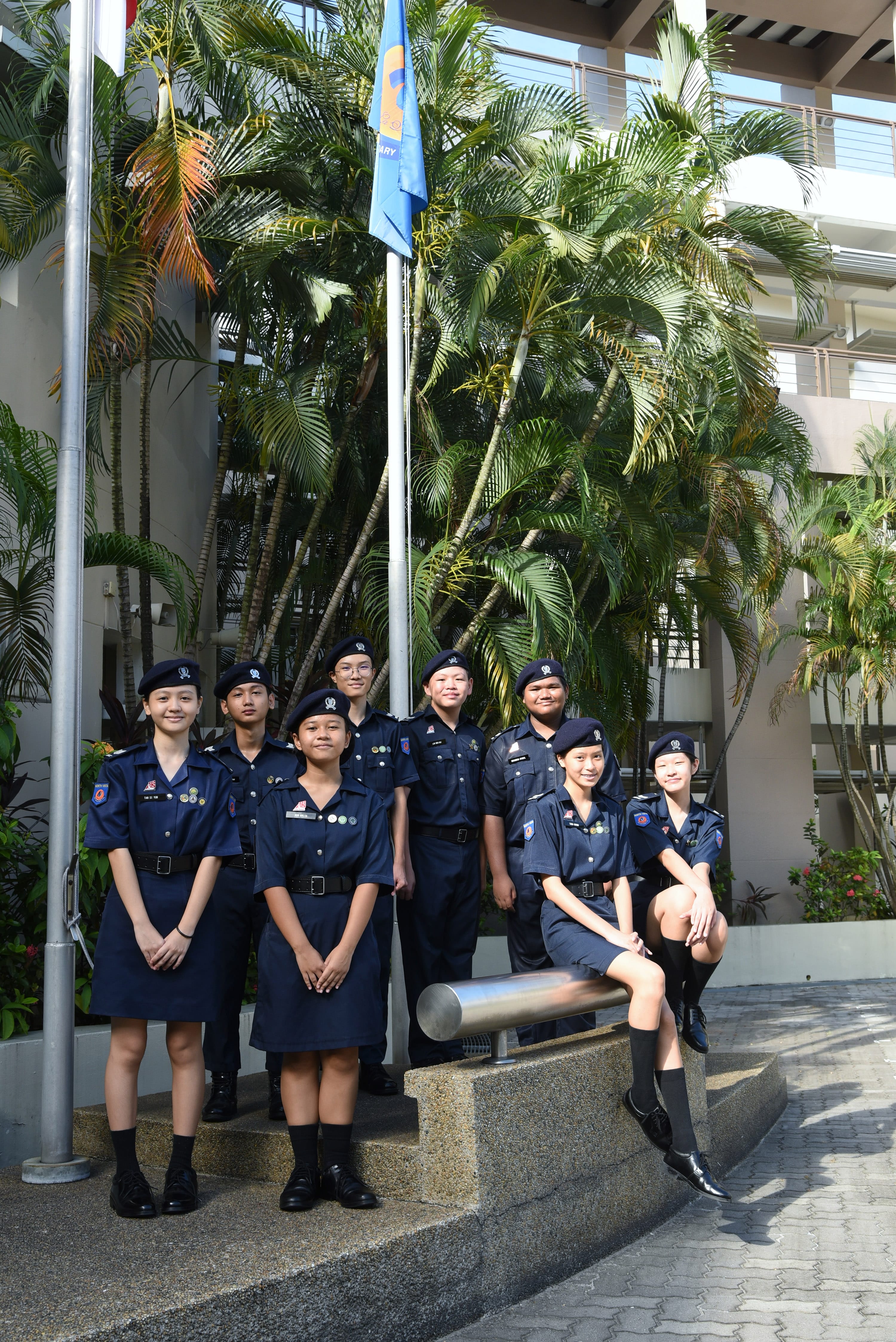 NV NPCC cadets in uniforms and berets pose near flagpoles a the school's parade square in front of the flag poles..