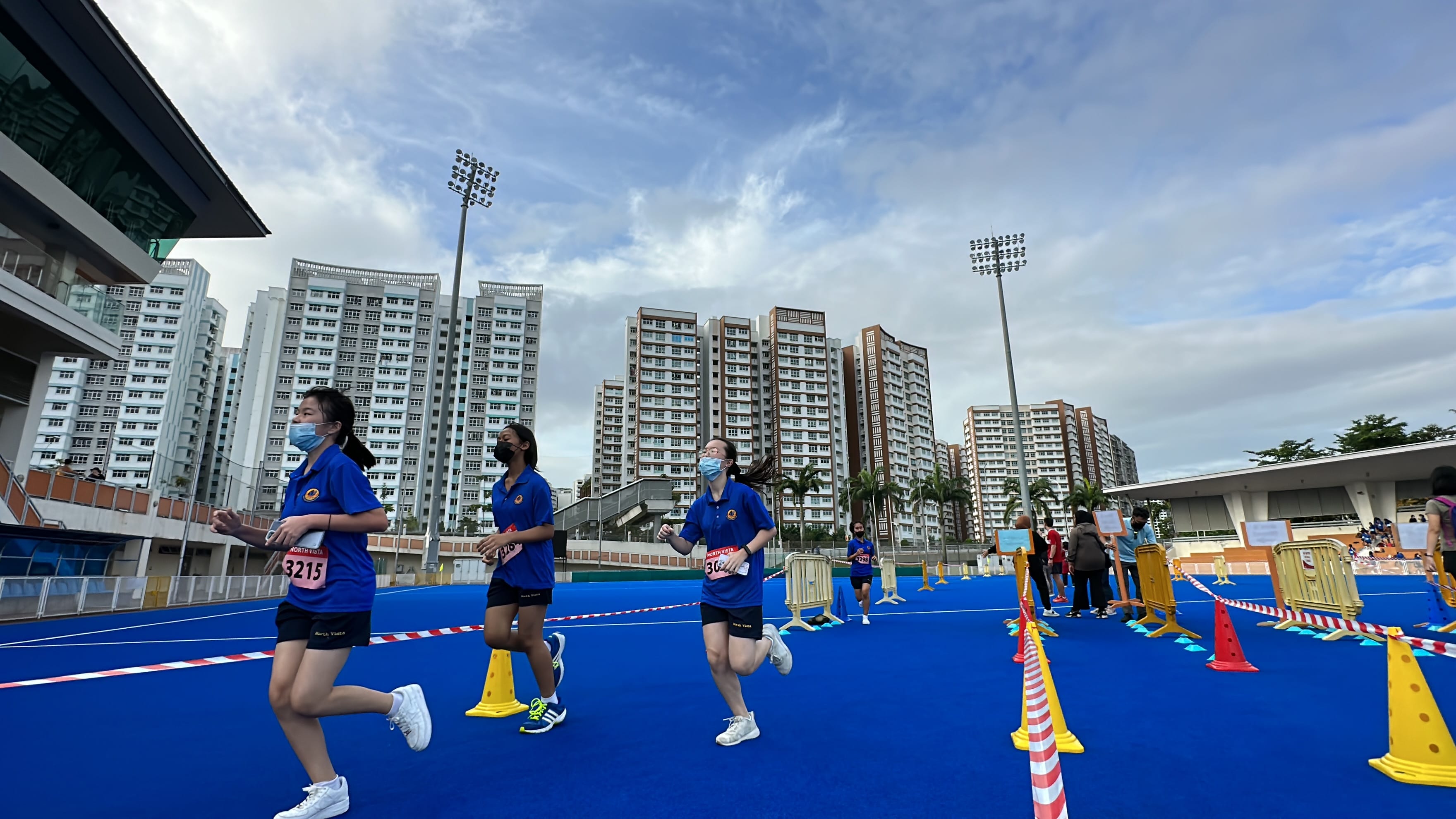 NV students with race bibs run on a blue outdoor track, hockey stadium in Sengkang