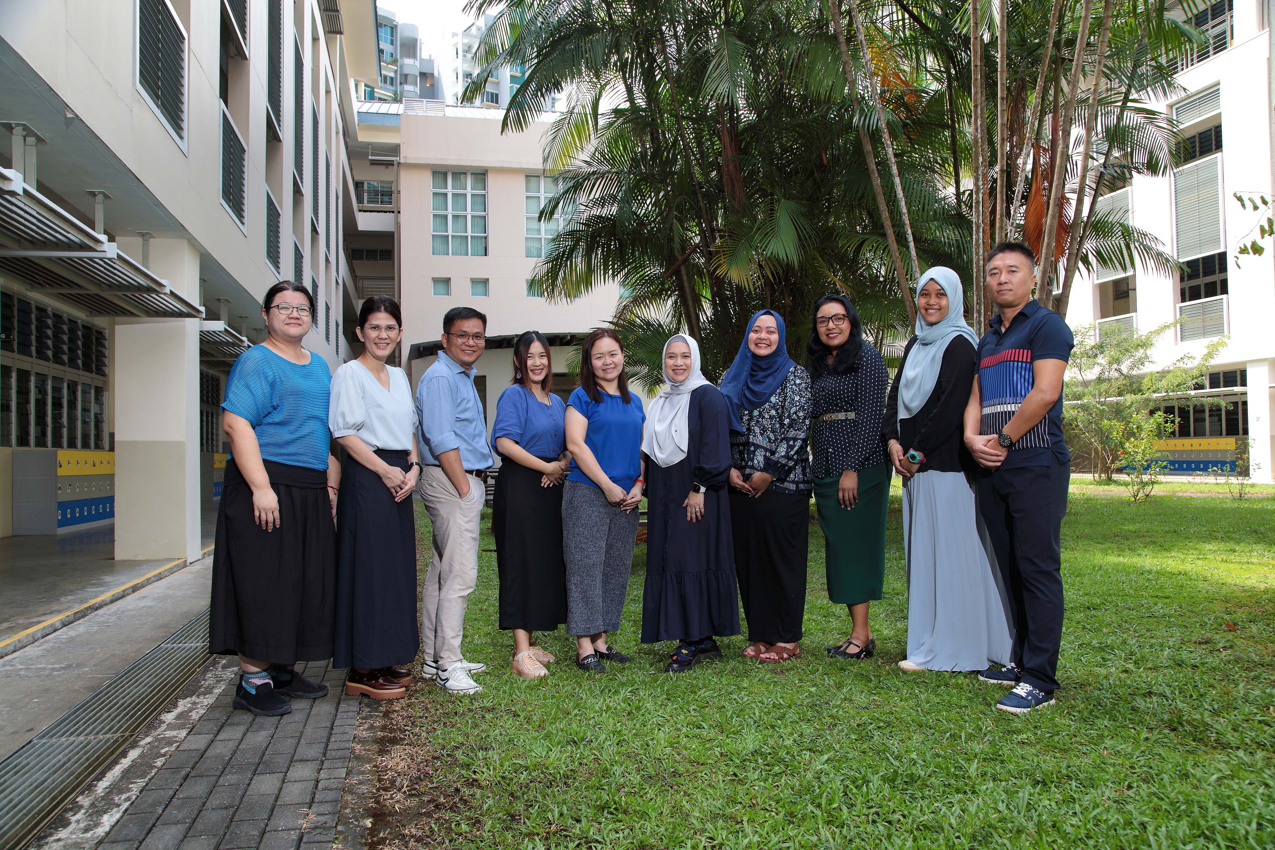 Mother Tongue Department staff standing together on a grass courtyard between classroom block.