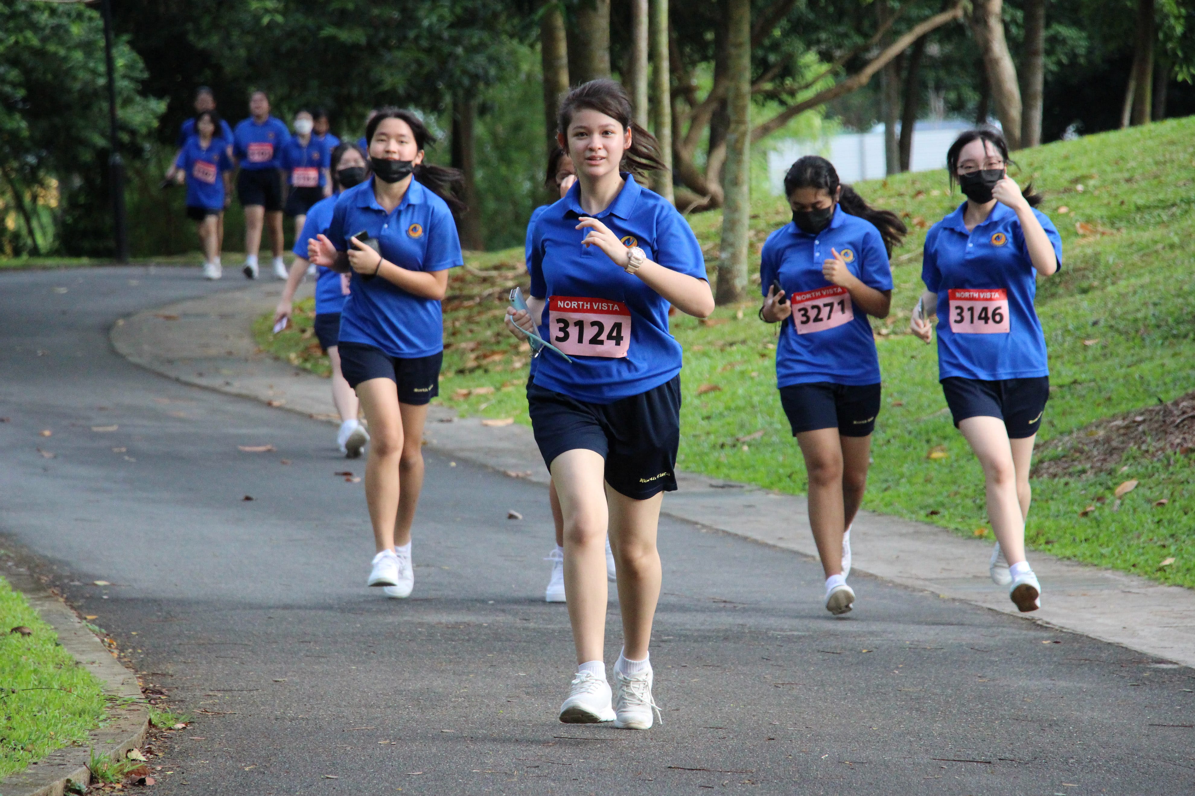 NV students with North Vista race bibs running along a tree-lined park path.