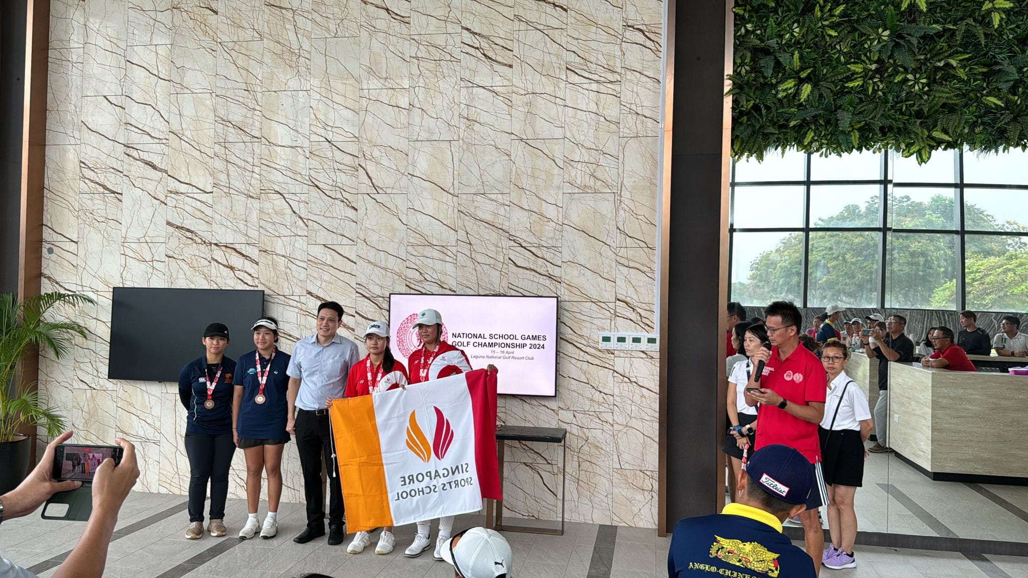 Group of NV student golfers posing with a Singapore Sports School flag at the 2024 National School Games Golf Championship.