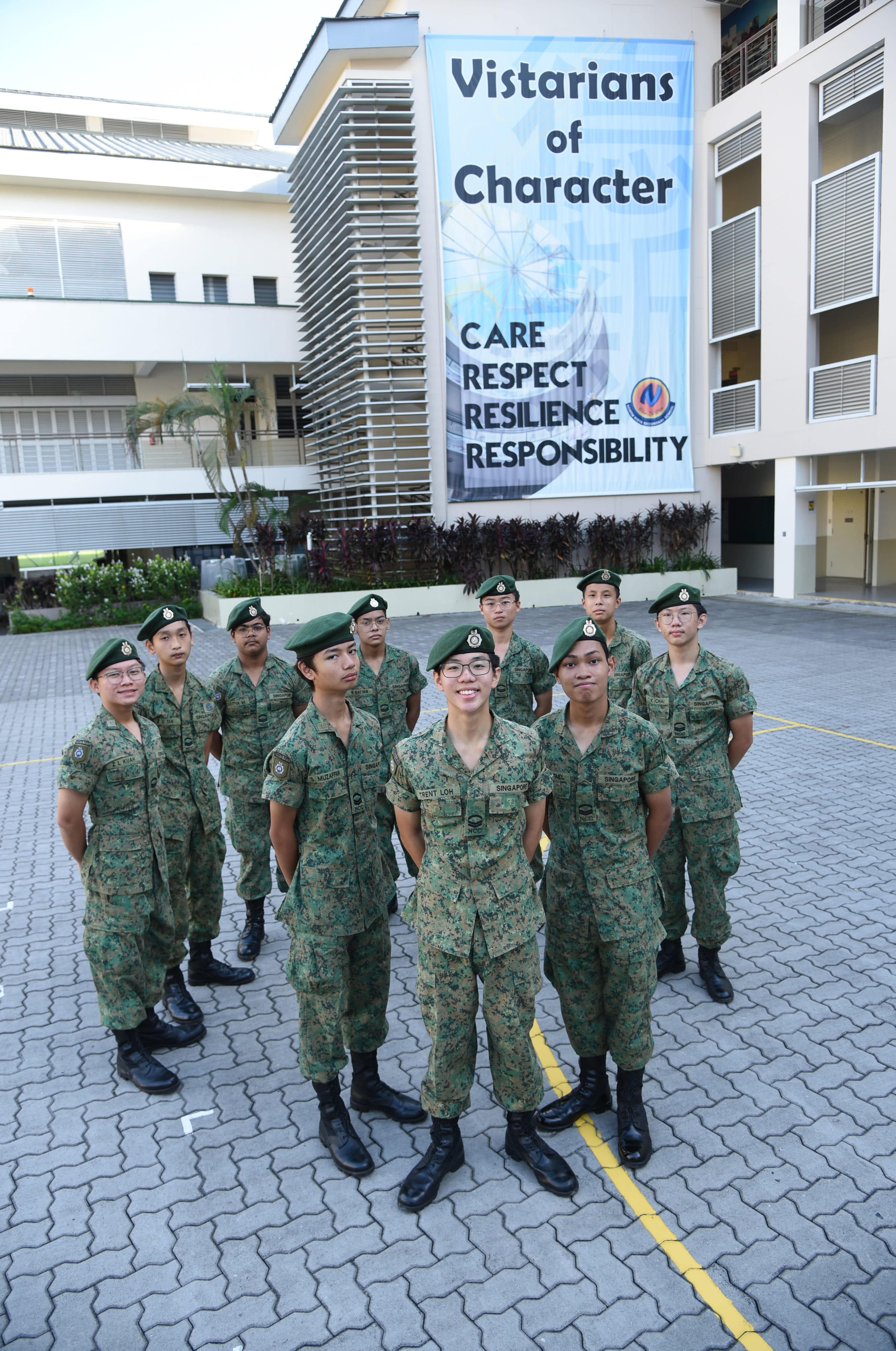 NV NCC cadets in uniforms and green berets stand in the school's parade square.