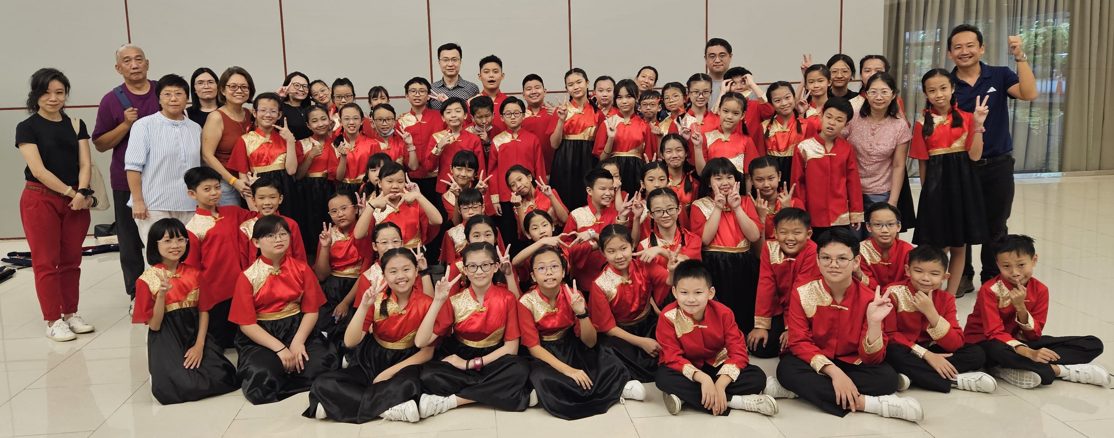 Large group of children in red and gold traditional Chinese costumes posing with adults, many making peace signs.