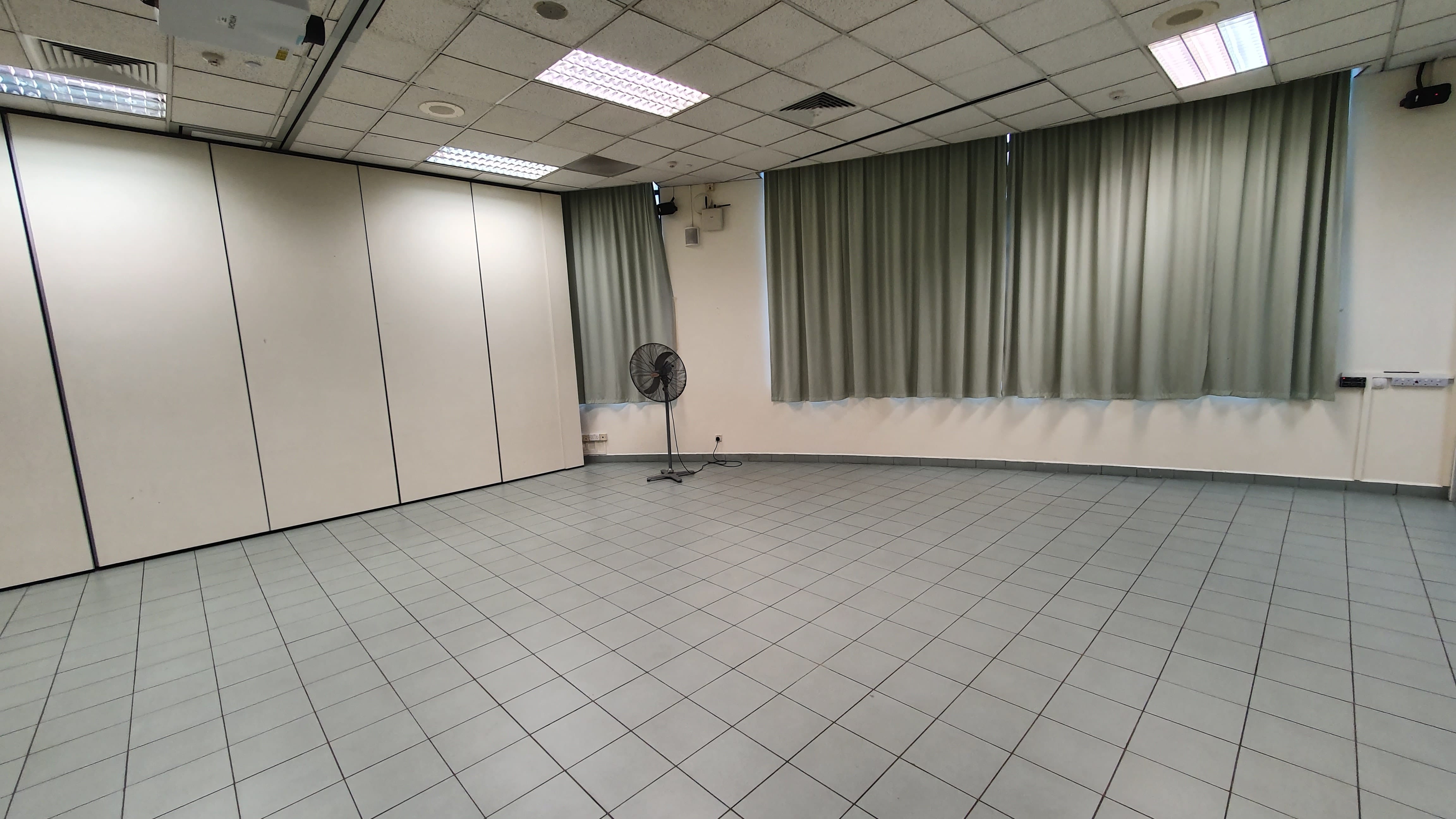 Empty room with tiled floor, gray curtains along the back wall, a standing fan, and white folding partition walls on the left.