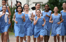 A group of smiling girls in matching light blue dresses running and laughing together outdoors.
