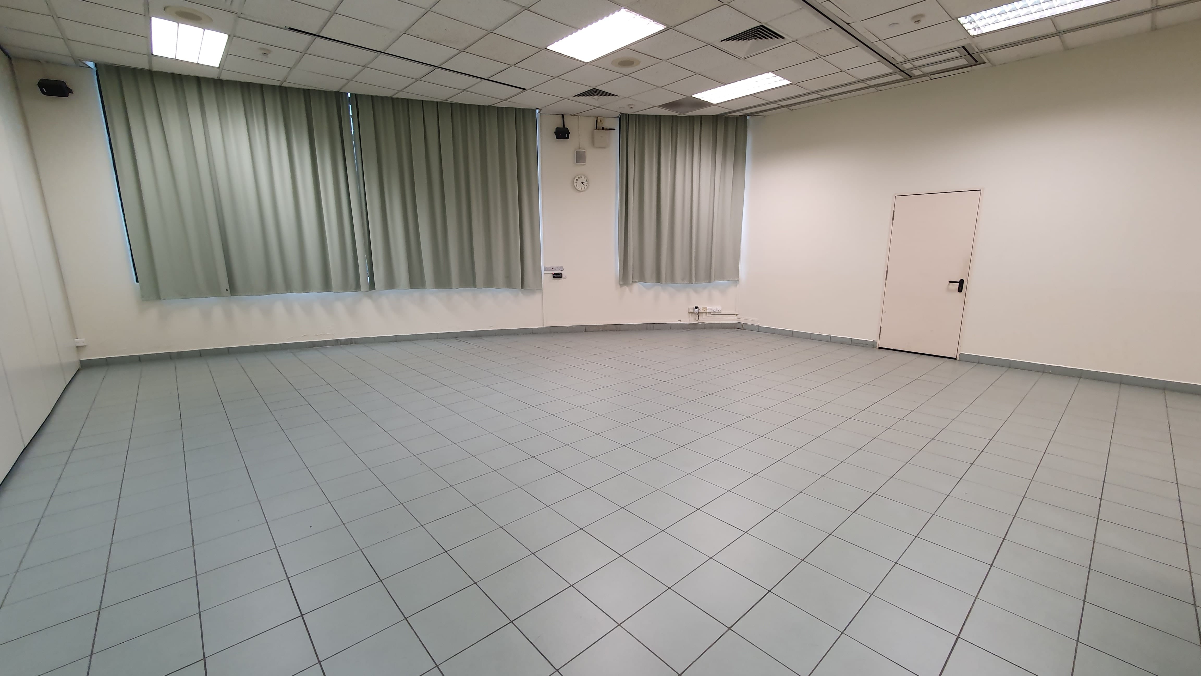 Empty room with gray tiled floor, white walls, gray curtains on windows, a wall clock, and a white door on the right.