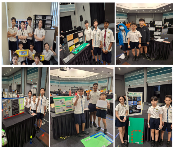 Students in school uniforms stand near project display boards at what appears to be a science fair or exhibition.