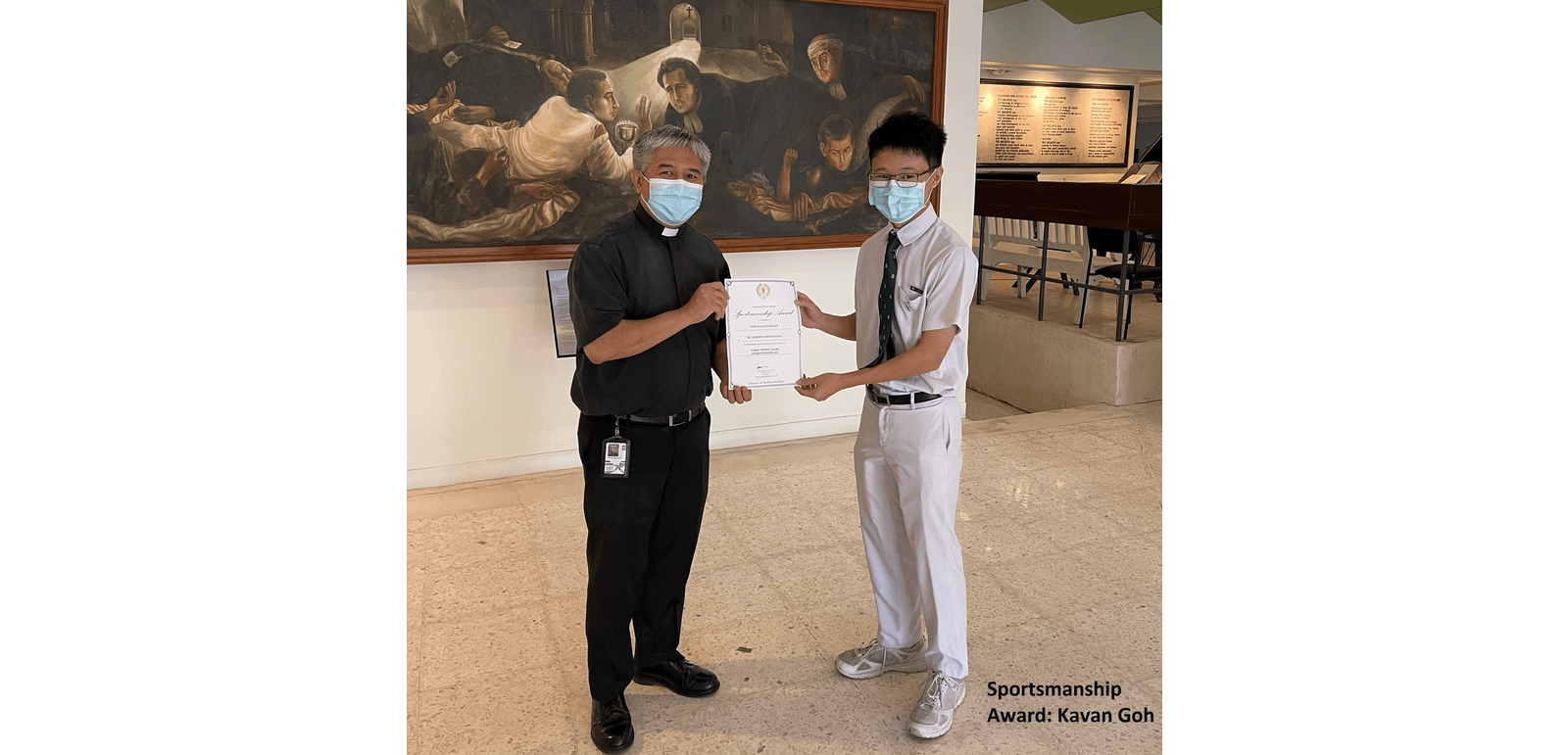 Two masked men hold a Sportsmanship Award certificate together indoors before a large painting.