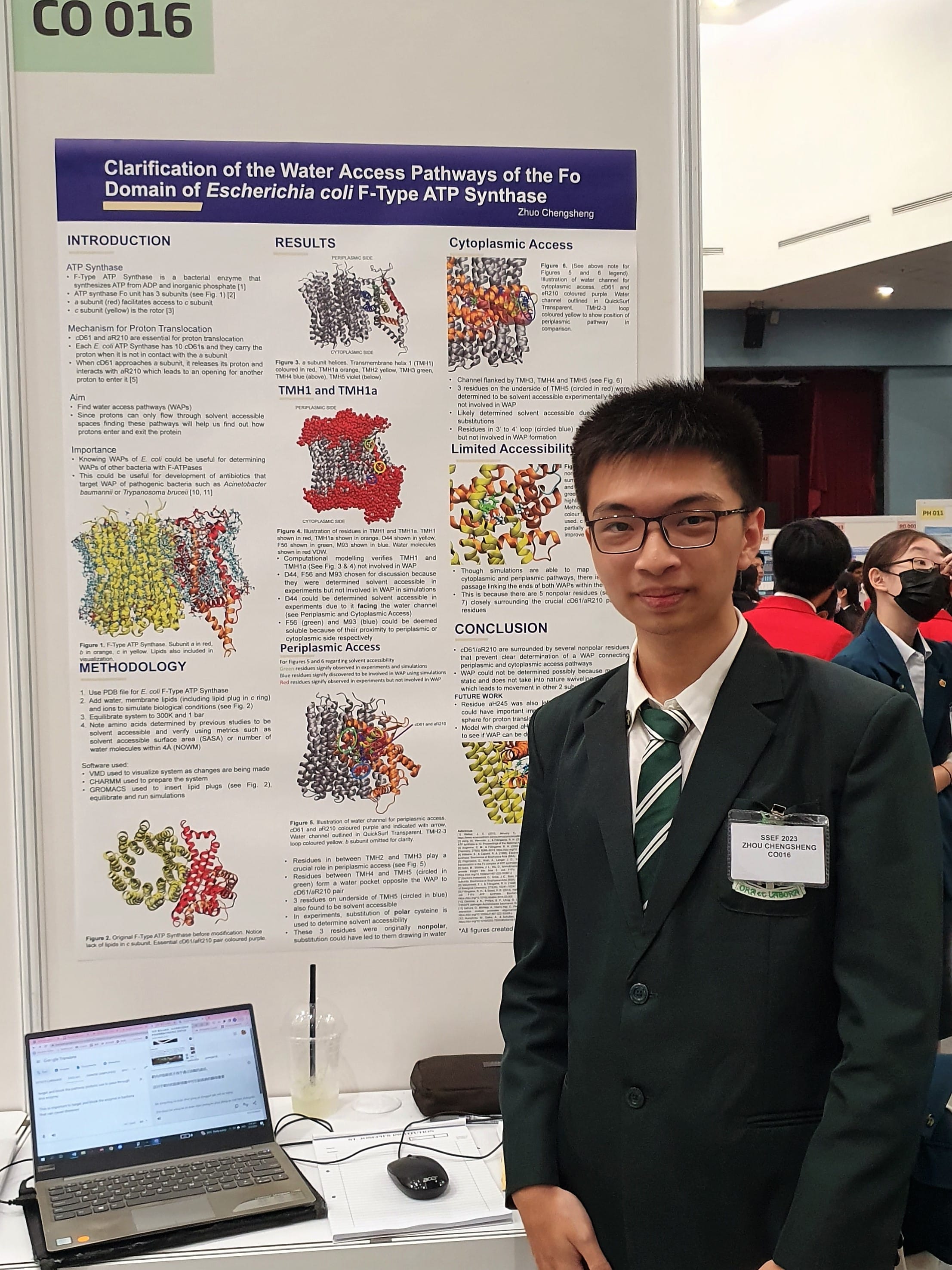 Zhou Chengsheng stands beside his SSEF poster on water access pathways in E. coli ATP synthase, board CO 016.