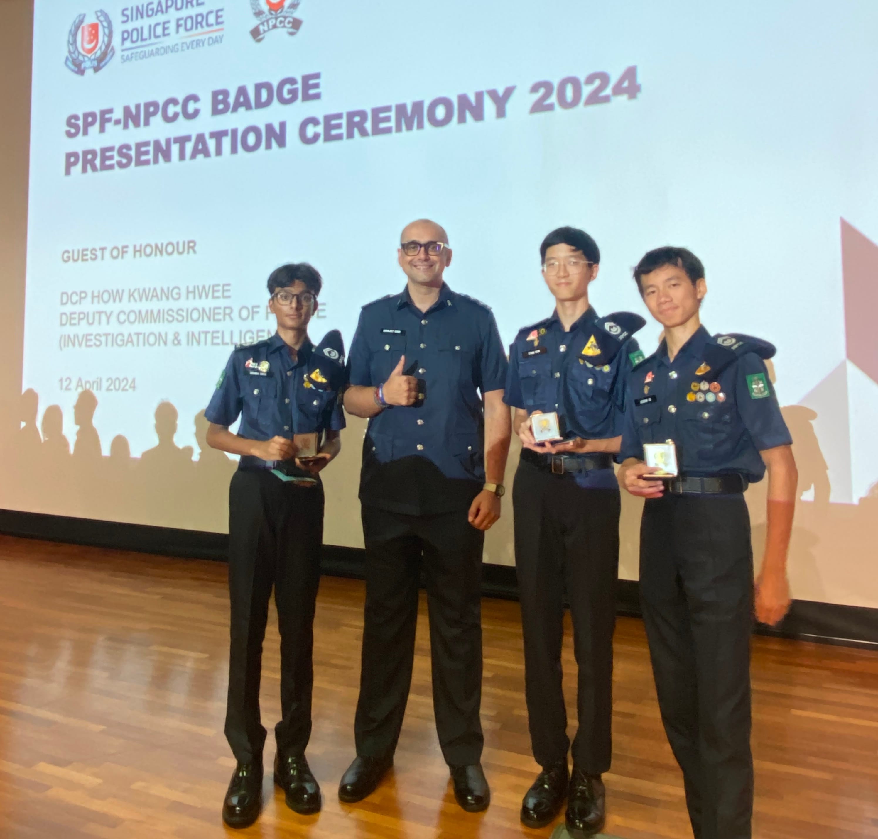 Four people in blue uniforms pose at the SPF-NPCC Badge Presentation Ceremony 2024, holding award boxes.