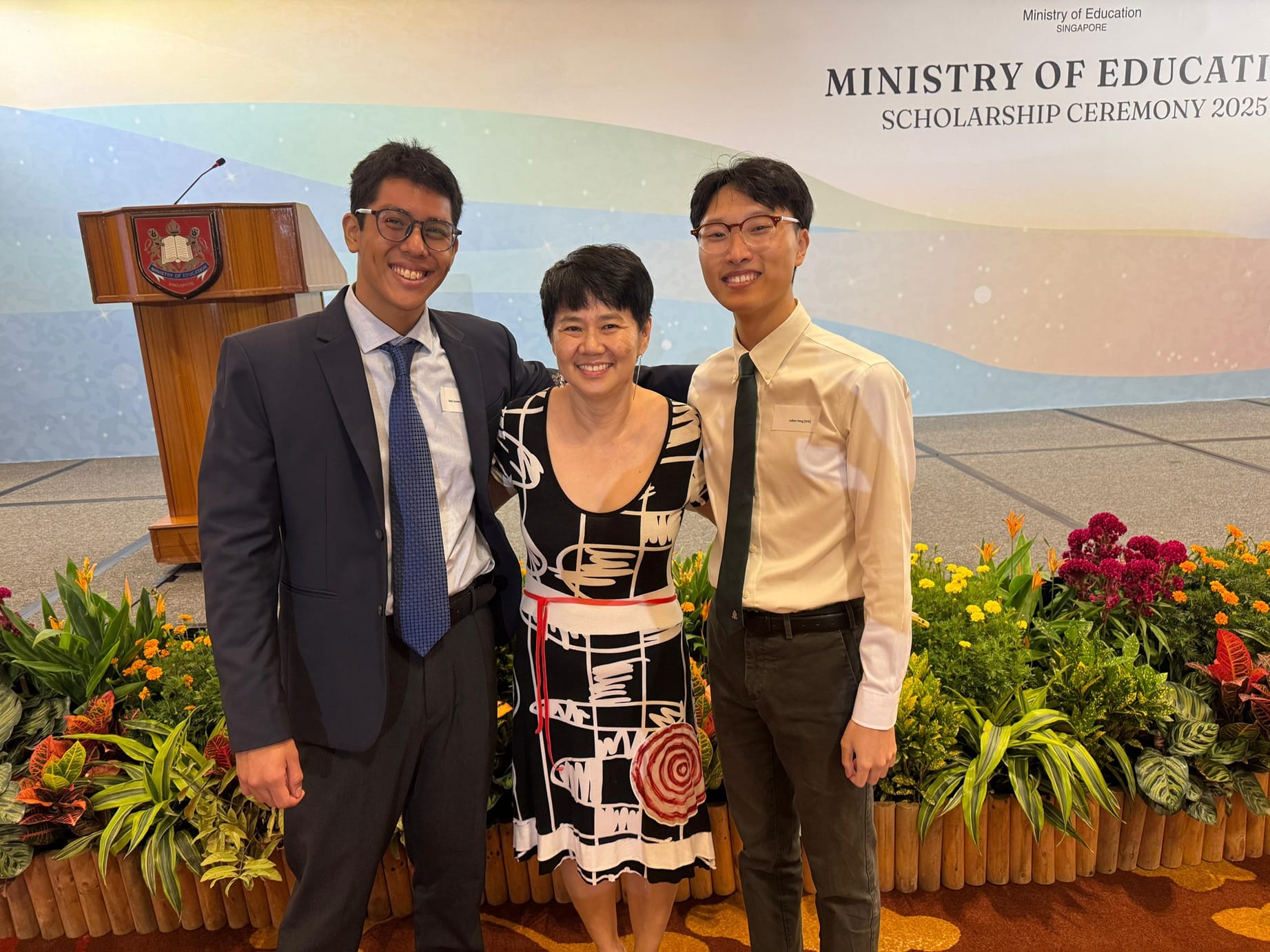 Three smiling people pose at the Ministry of Education Singapore Scholarship Ceremony 2025 banner.